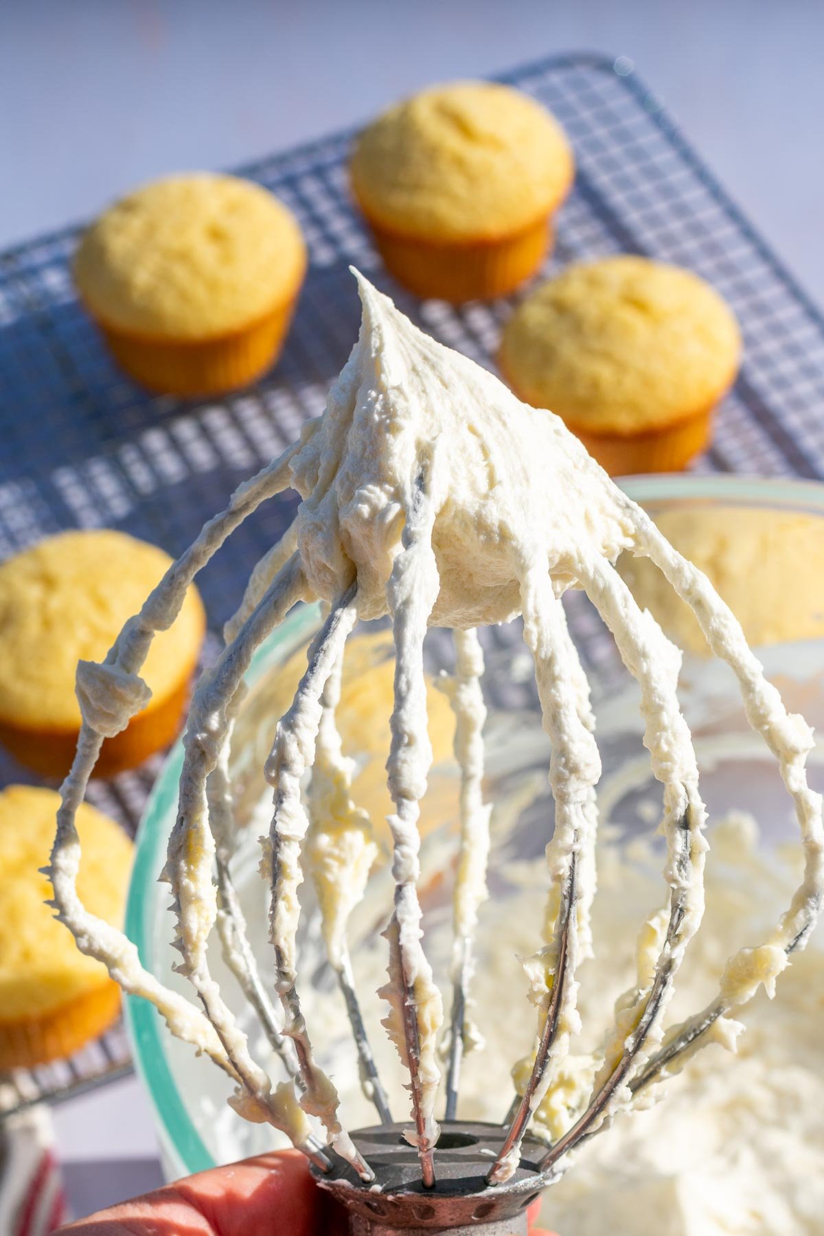 Sourdough frosting on a whisk attachment with unfrosted cupcakes in the background.