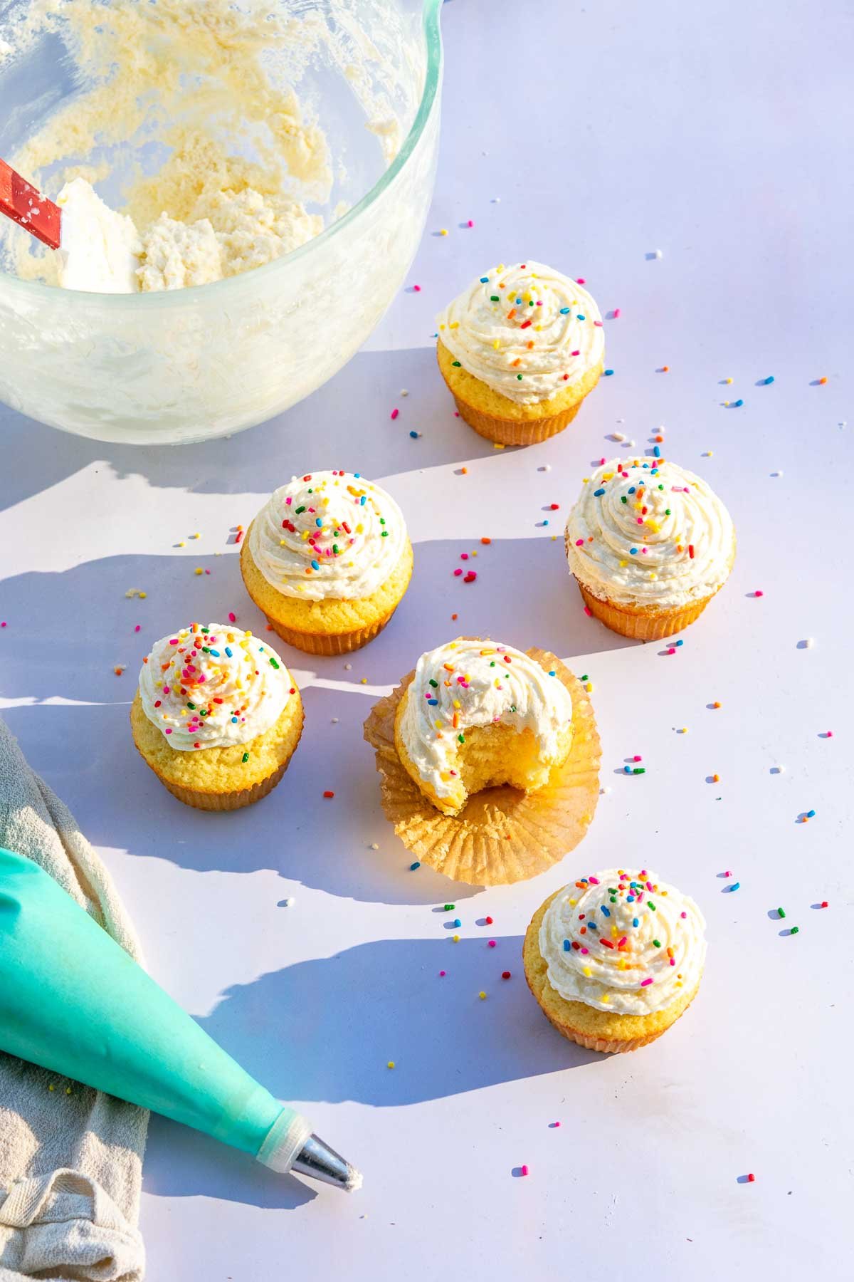 Sourdough frosting on vanilla cupcakes with rainbow sprinkles and a piping bag.