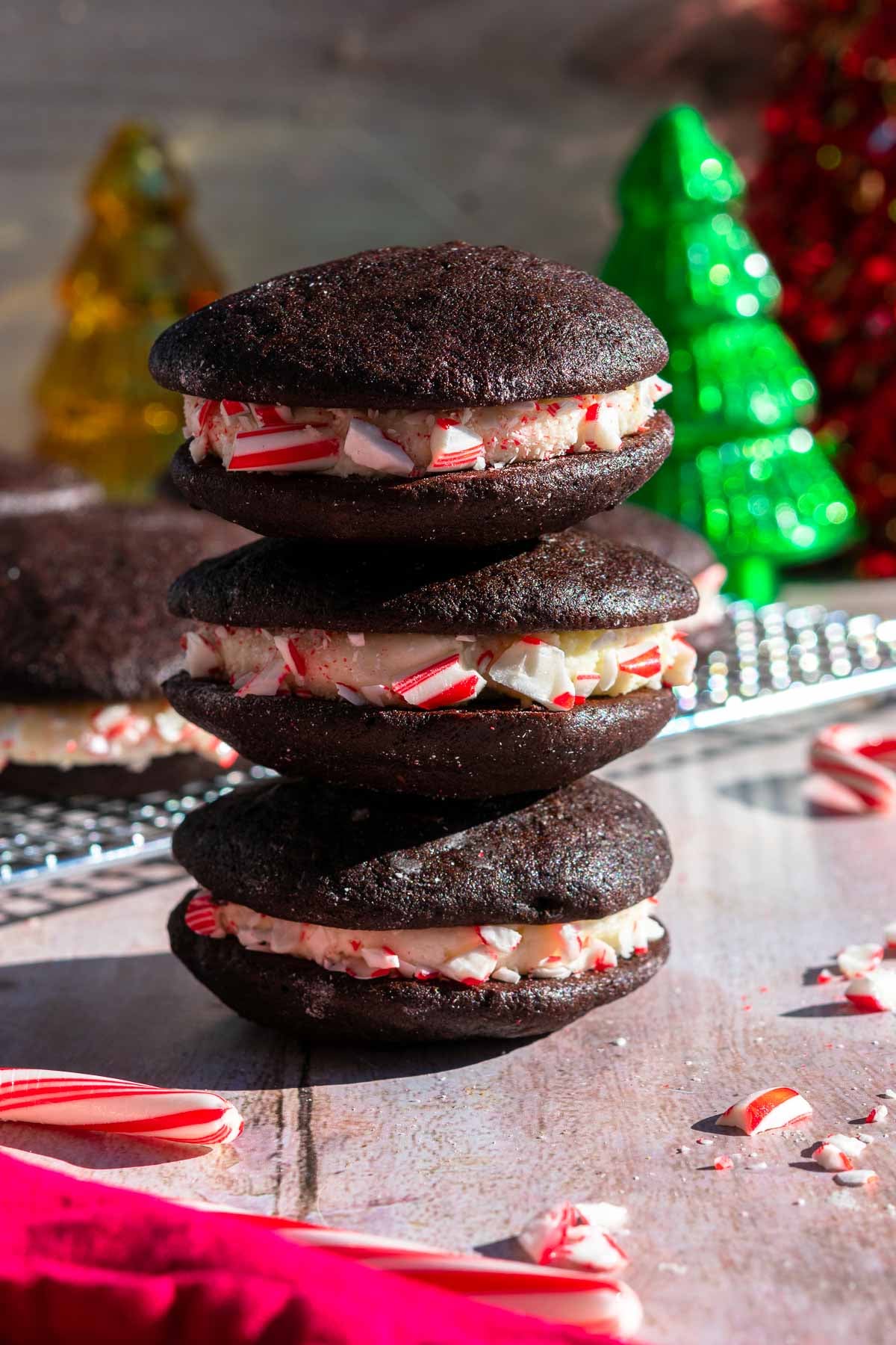 Three sourdough chocolate peppermint whoopie pies stacked on top of each other with christmas trees in the background.