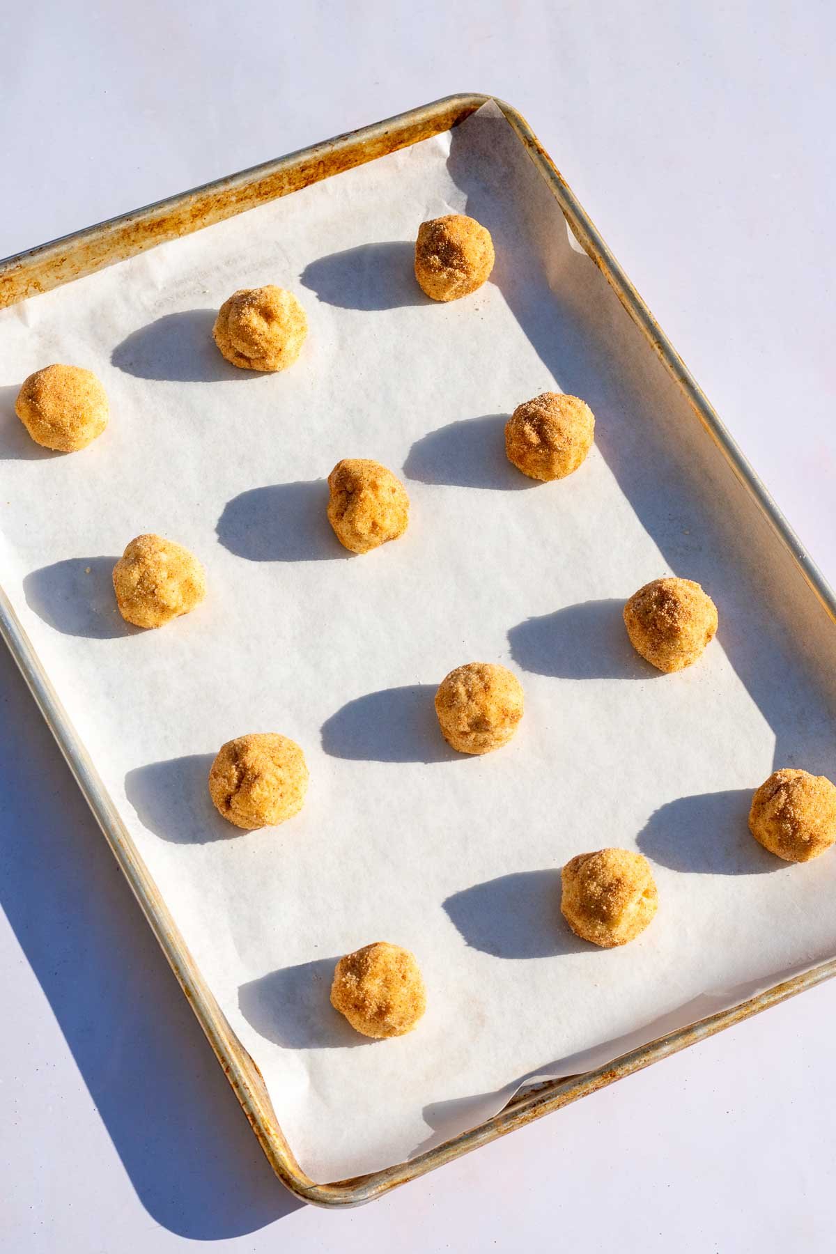 Twelve unbaked sourdough snickerdoodle cookie balls on a baking sheet lined with parchment paper.