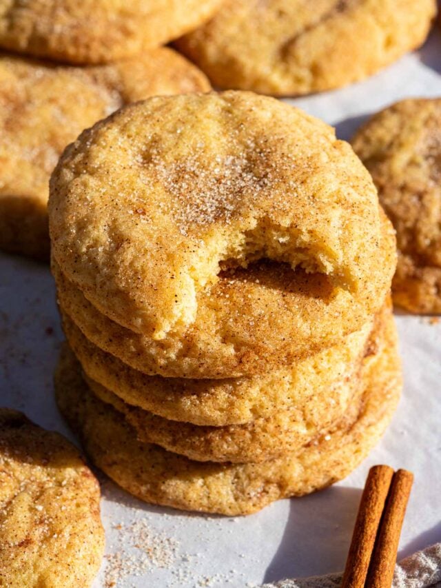 Stack of sourdough snickerdoodle cookies with the bite taken out of the top one and a cinnamon stick.