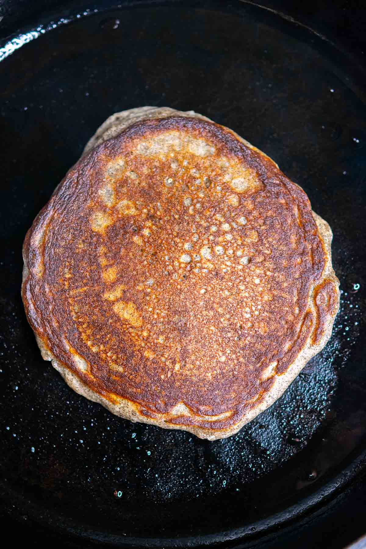 Flipped and cooked sourdough buckwheat pancake in a cast iron skillet with crispy edges.