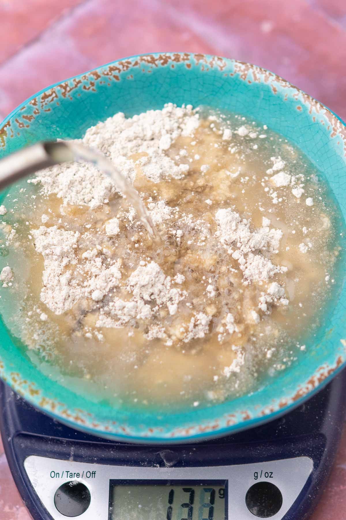 Pouring boiling water into a bowl of rye flour on a kitchen scale for the yudane.
