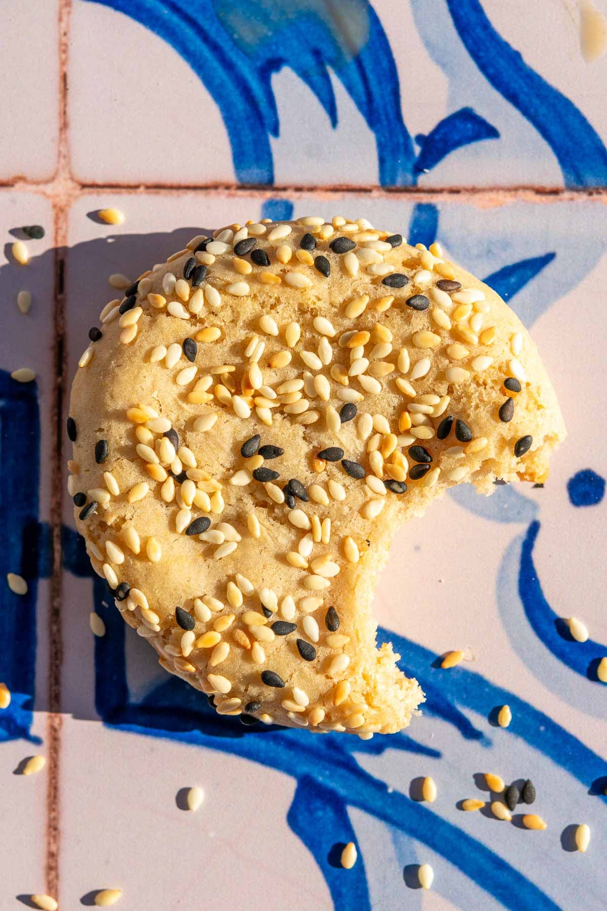 Bite taken out of a sourdough tahini honey cookie with white and black sesame seeds.