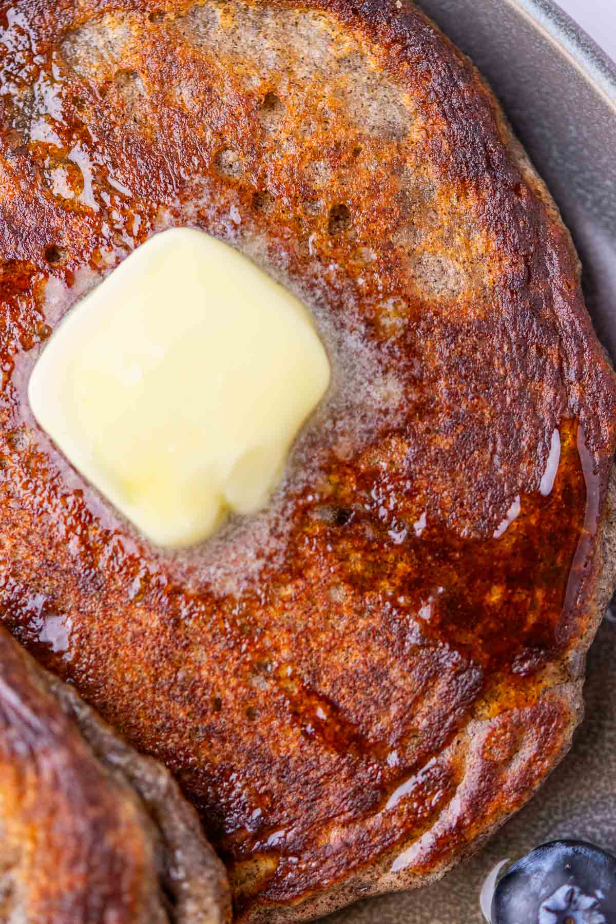 Up close of sourdough buckwheat pancakes with crispy edges, with a drizzle of maple syrup, and slightly melted butter.