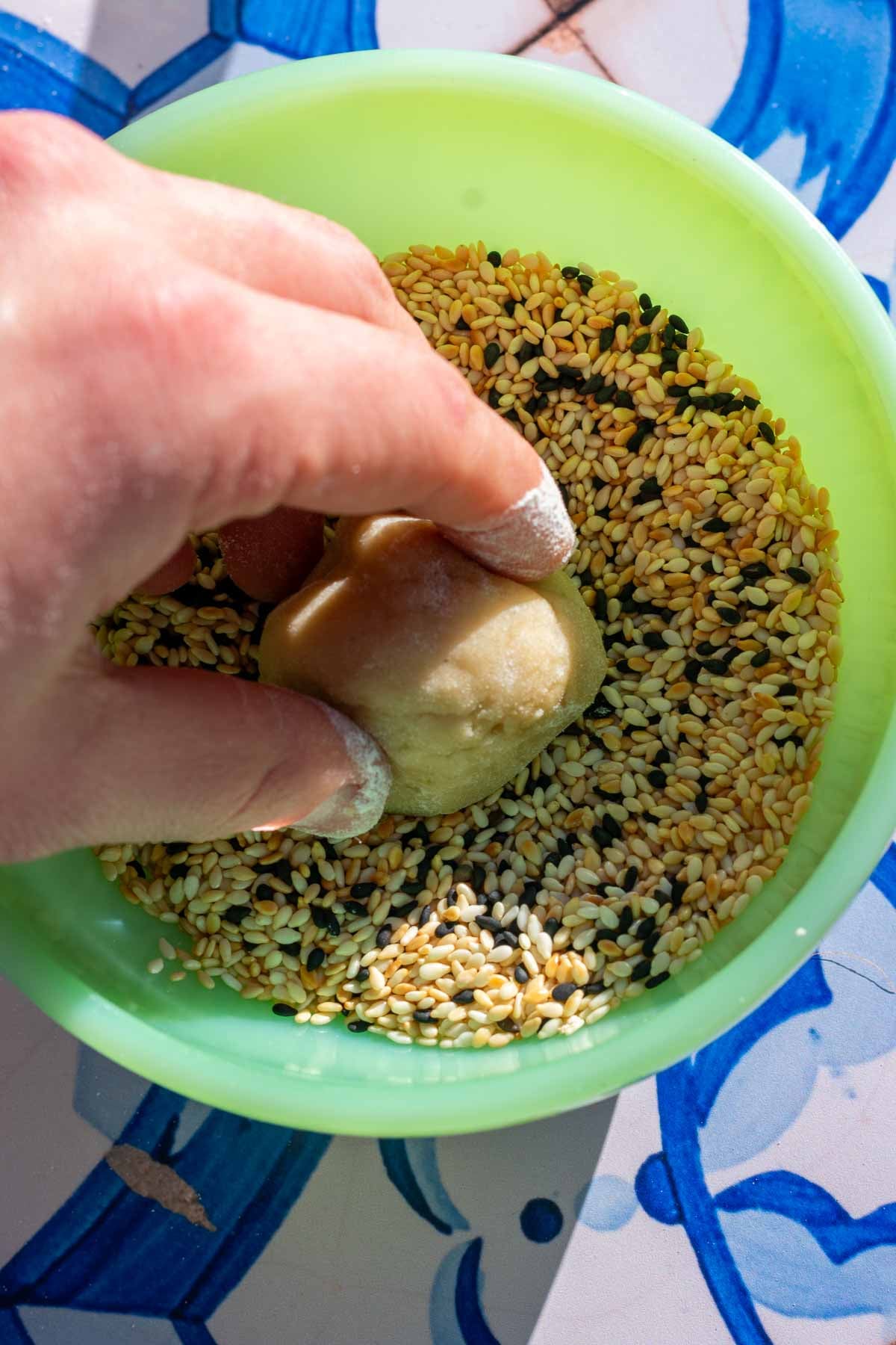 Dipping a ball of sourdough tahini cookie dough in sesame seeds.