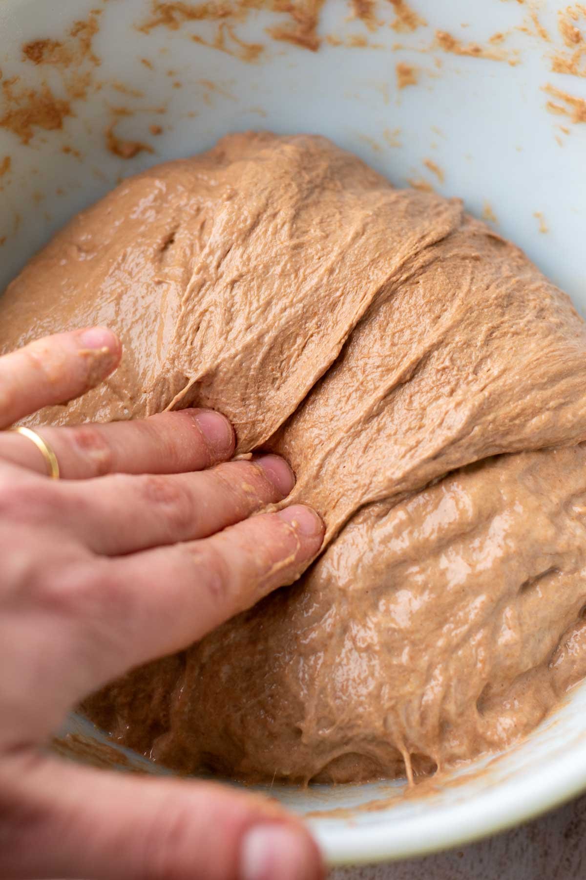 Stretch and folding chocolate coffee sourdough bread in bowl.