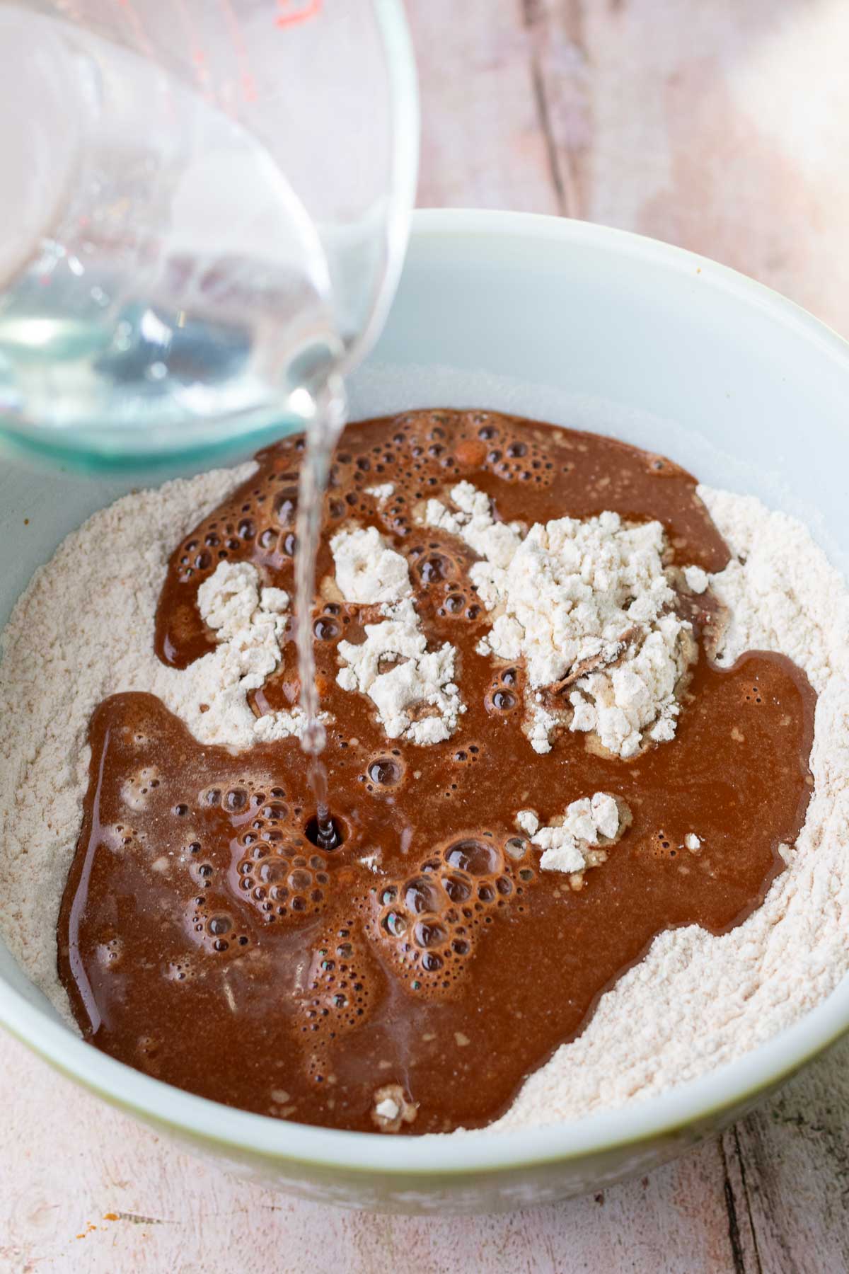 Pouring water into bowl of flour, coffee, and bloomed cocoa powder for autolyse.