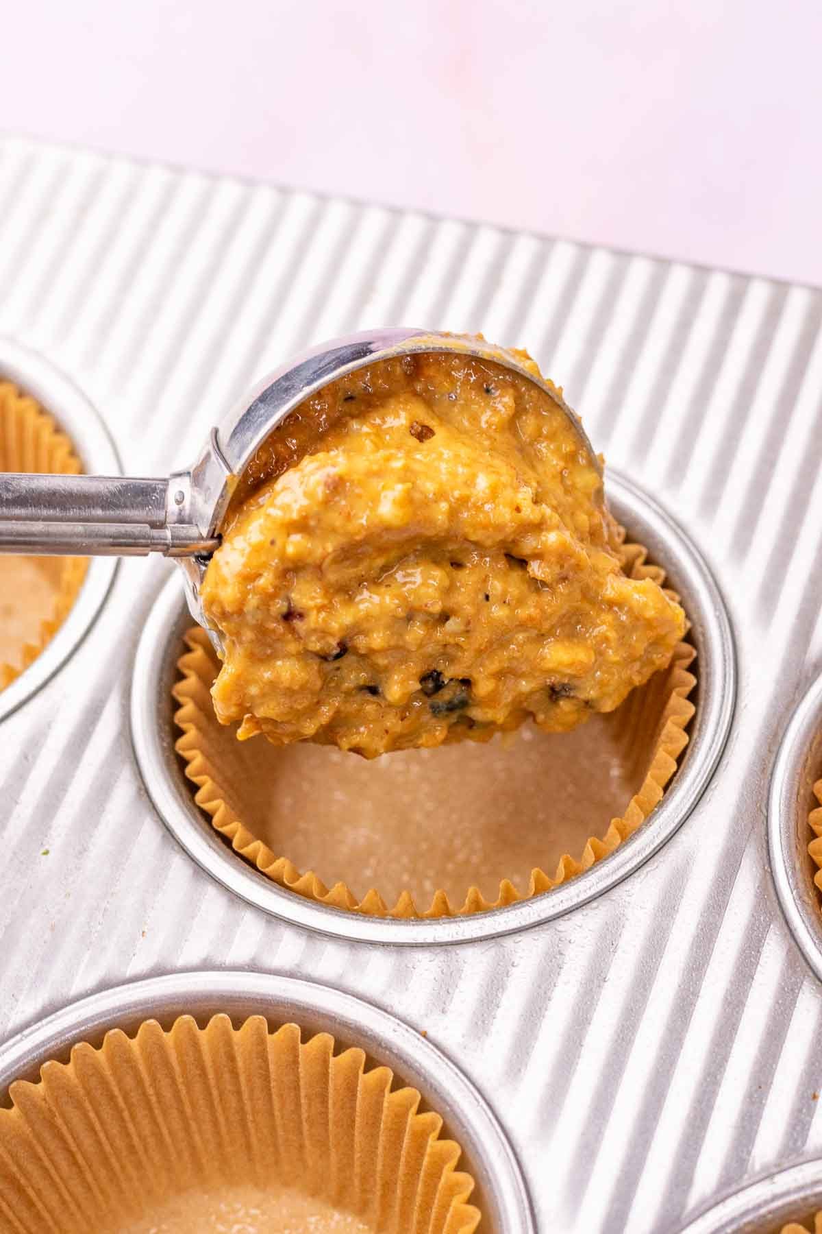Scooping sourdough bran muffin batter into a lined muffin pan with a cookie scoop.