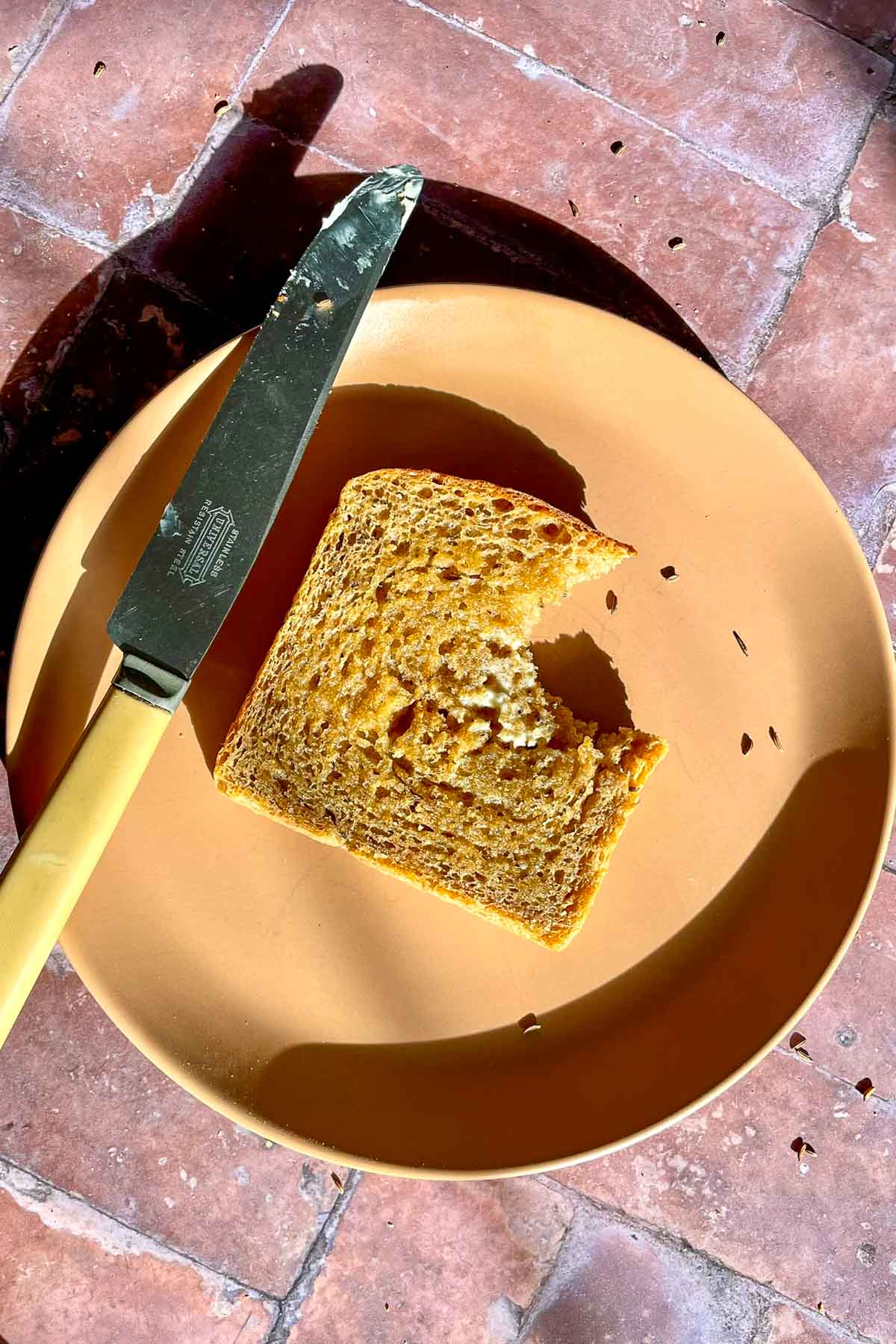 Slice of sourdough rye sandwich bread with butter and a bite taken out of it on a plate with a butter knife.