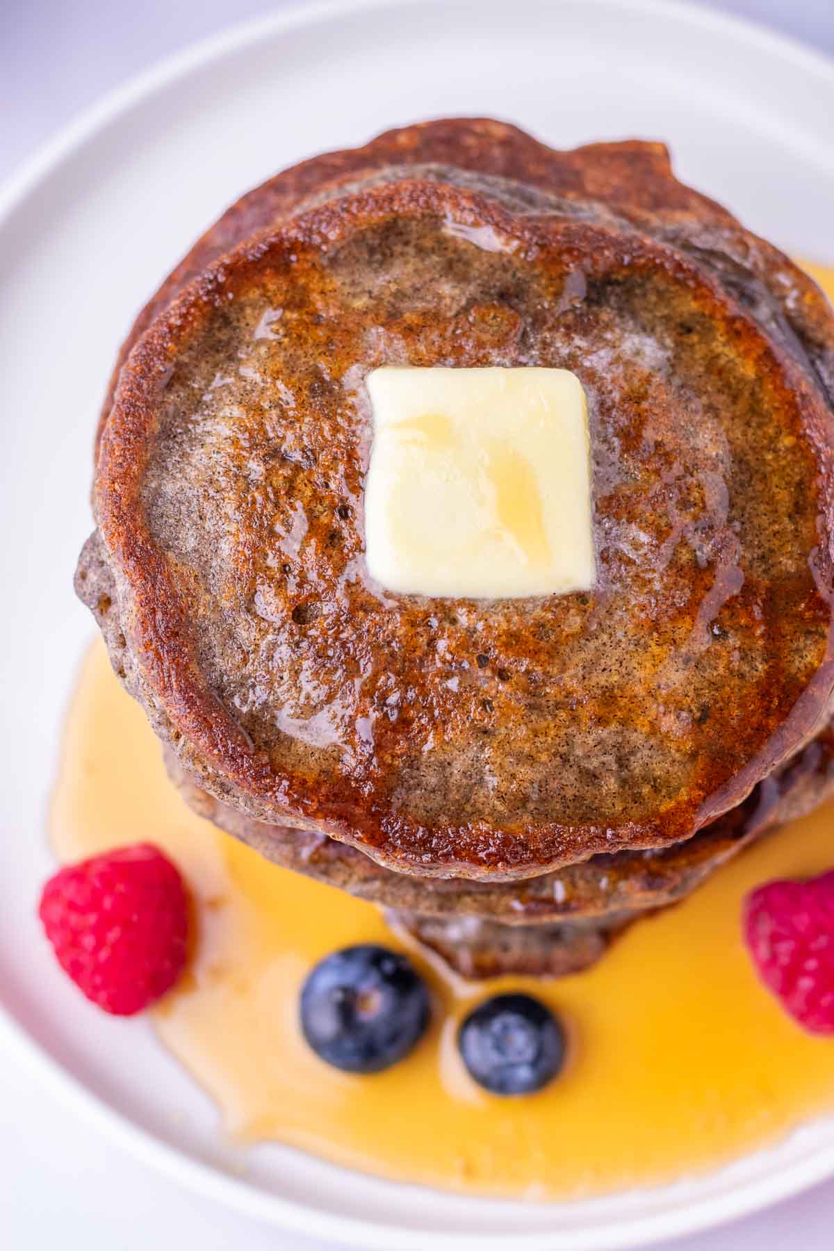 Top of a stack of sourdough buckwheat pancakes on a plate with melted butter and maple syrup.