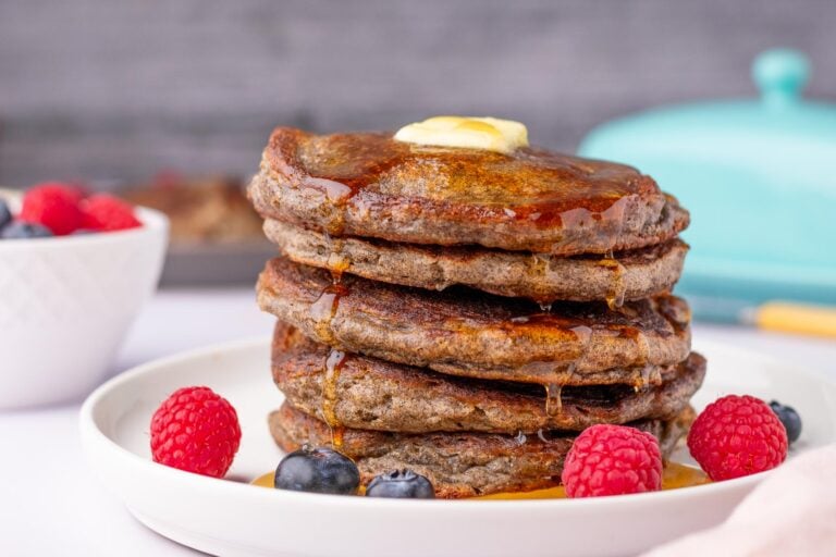 Stack of sourdough buckwheat pancakes with raspberries, blueberries, maple syrup, and butter.