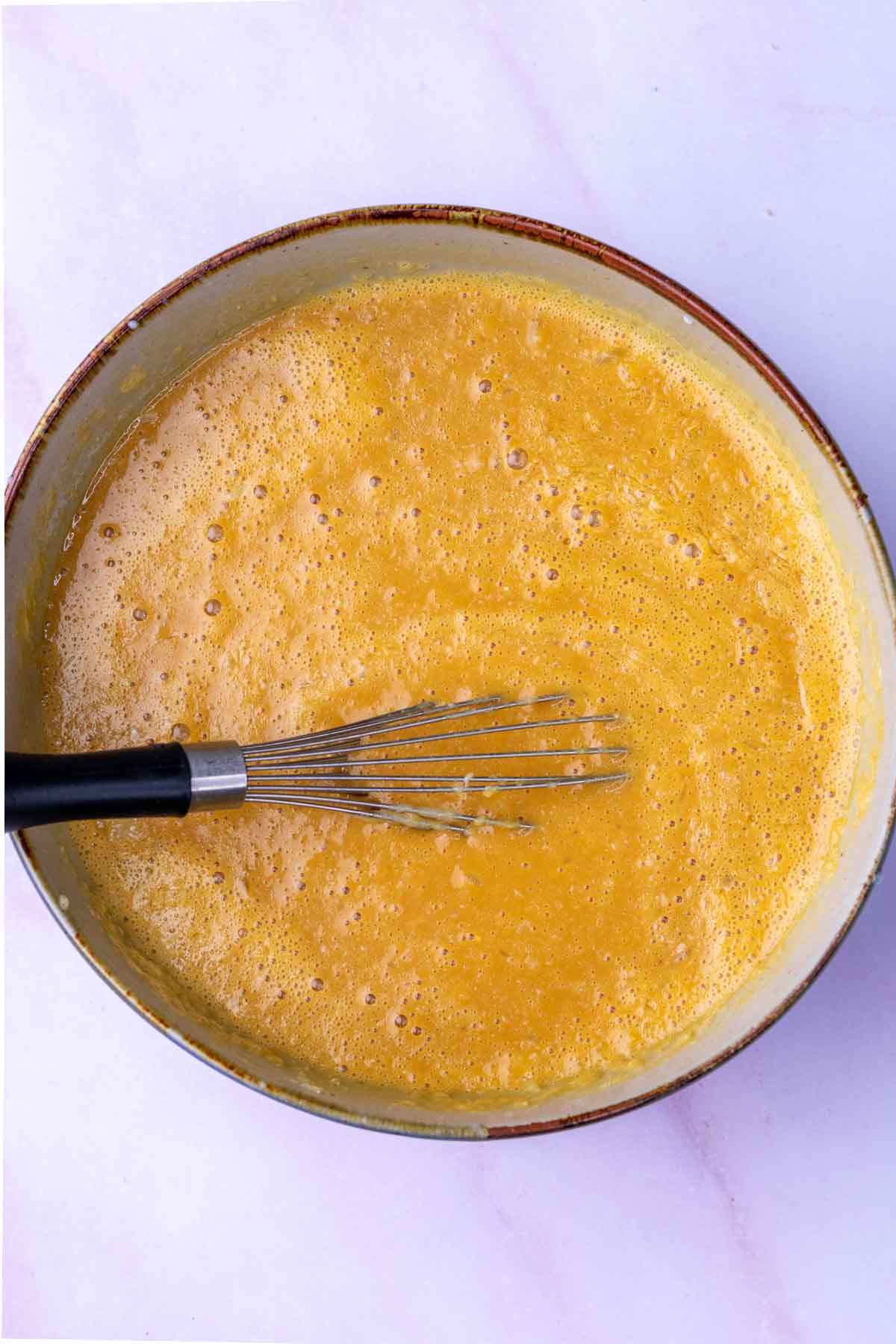 Bowl of mixed wet ingredients for sourdough bran muffins with a whisk.