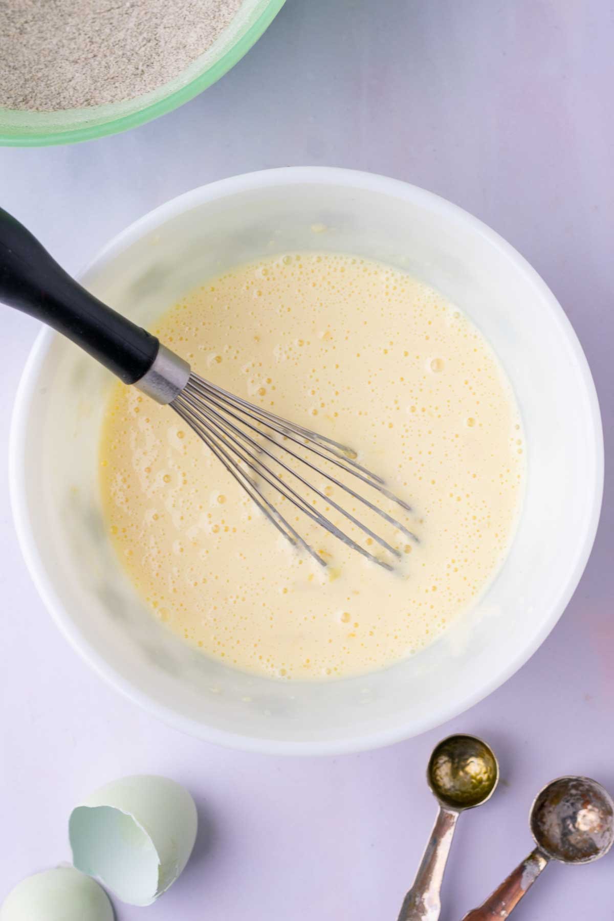 Bowl of wet ingredients for sourdough buckwheat pancakes with a whisk.