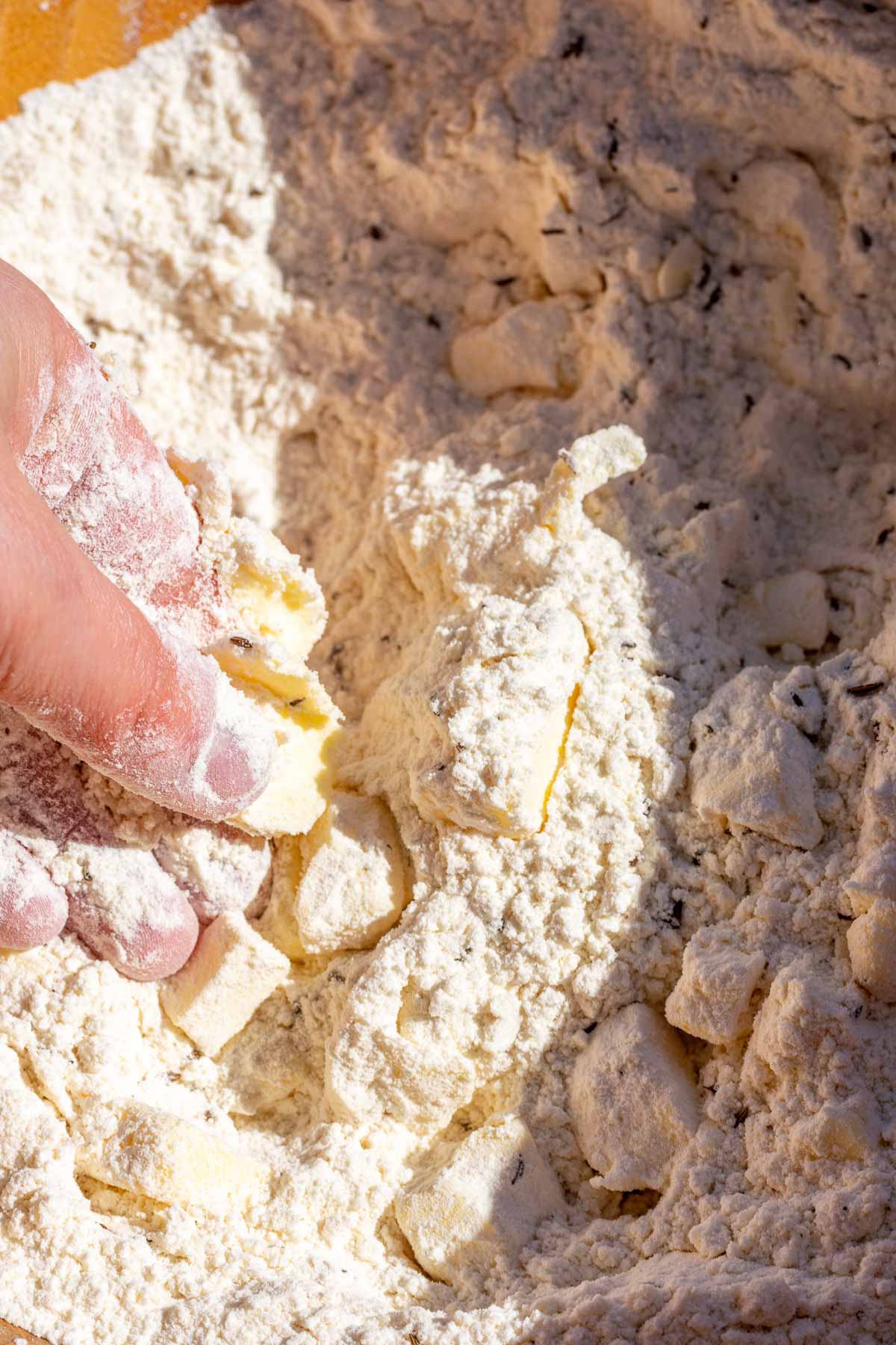Hand in bowl of dry ingredients mixing in butter.