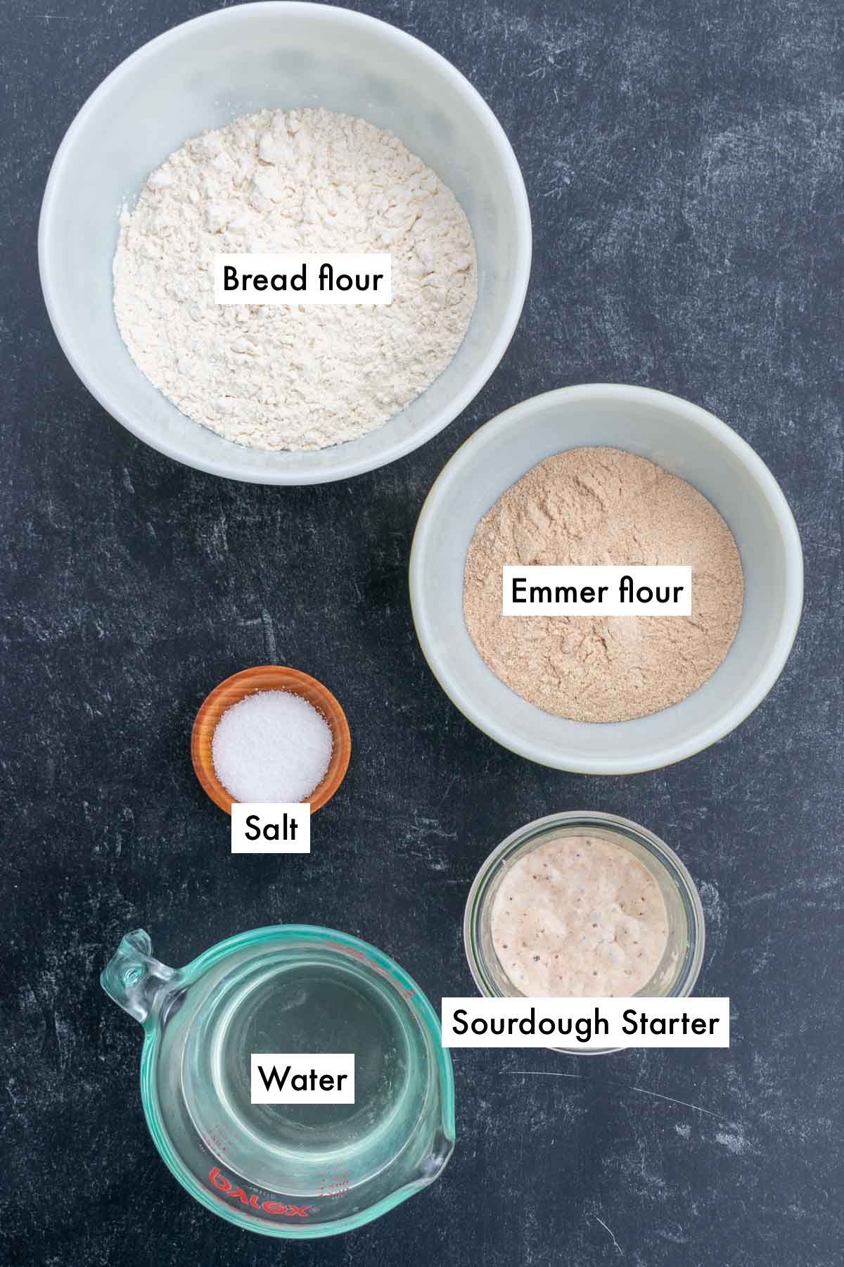 Labeled bowls of ingredients needed for emmer sourdough bread including bread flour, emmer flour, water, salt, and sourdough starter.