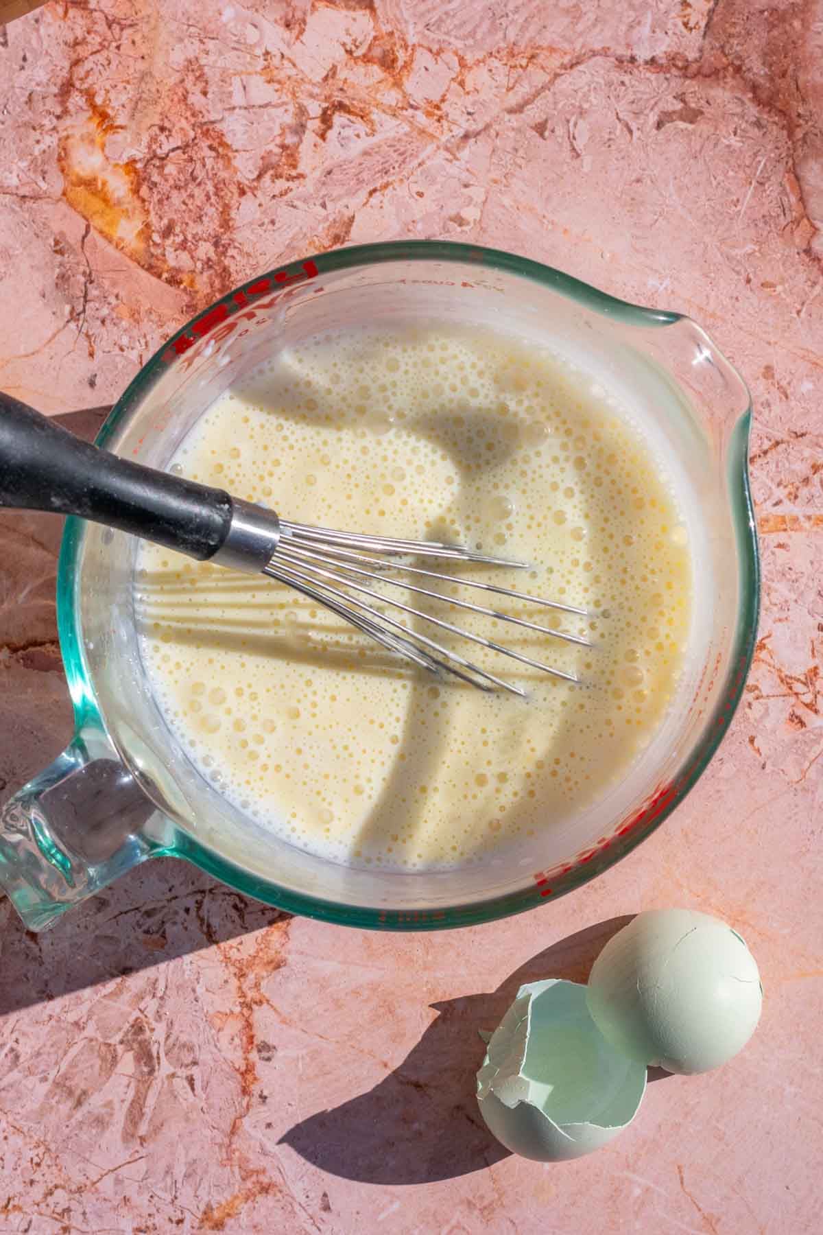 Mixed wet ingredients for sourdough Irish soda bread with a whisk in a liquid measuring cup.