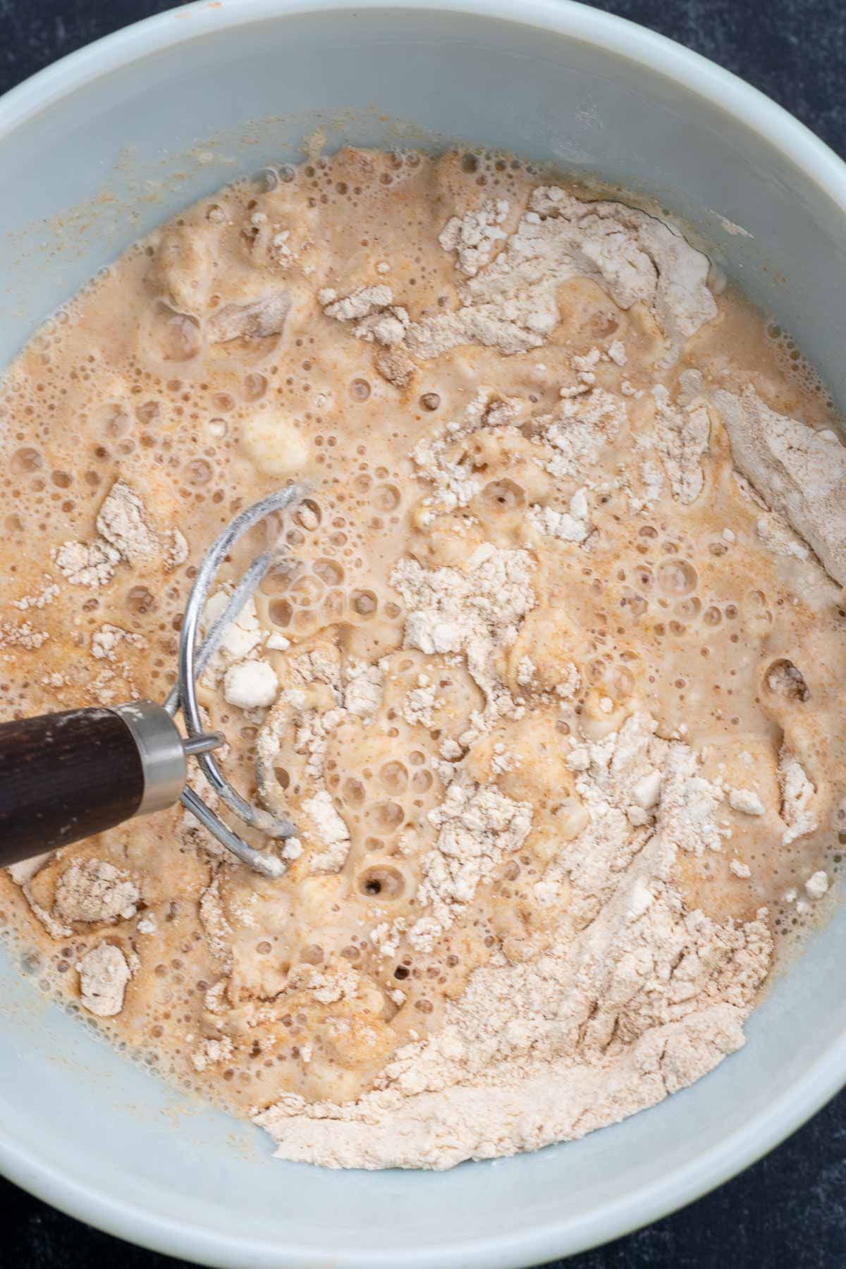 Mixing emmer and bread flour and water together in a bowl with a dough whisk.