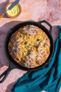 Sourdough Irish soda bread with raisins and caraway seeds in a cast-iron skillet and a bowl of butter.