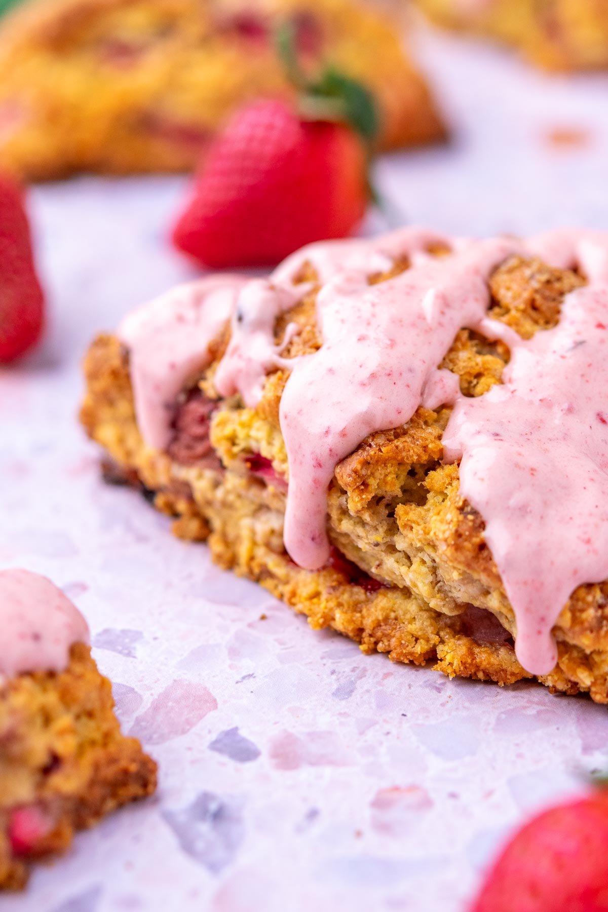 Close up of a sourdough strawberry scone with strawberry glaze and fresh strawberries.