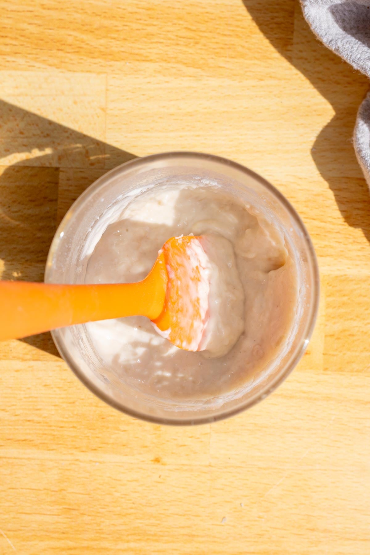Stirring dried sourdough starter, flour, and water with a silicone spatula in a glass jar to reactivate it.