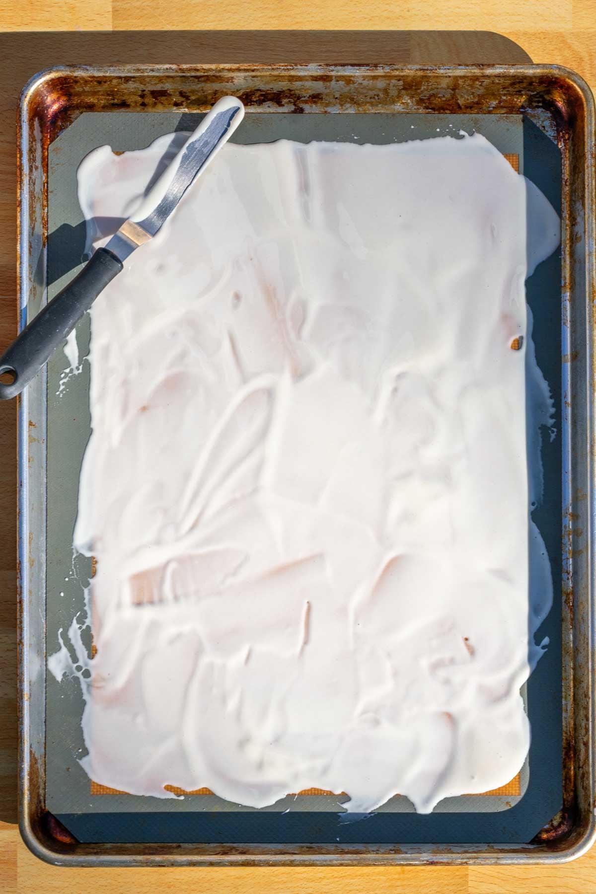 Sourdough starter spread thinly all on top of a silicone baking mat with an offset spatula.