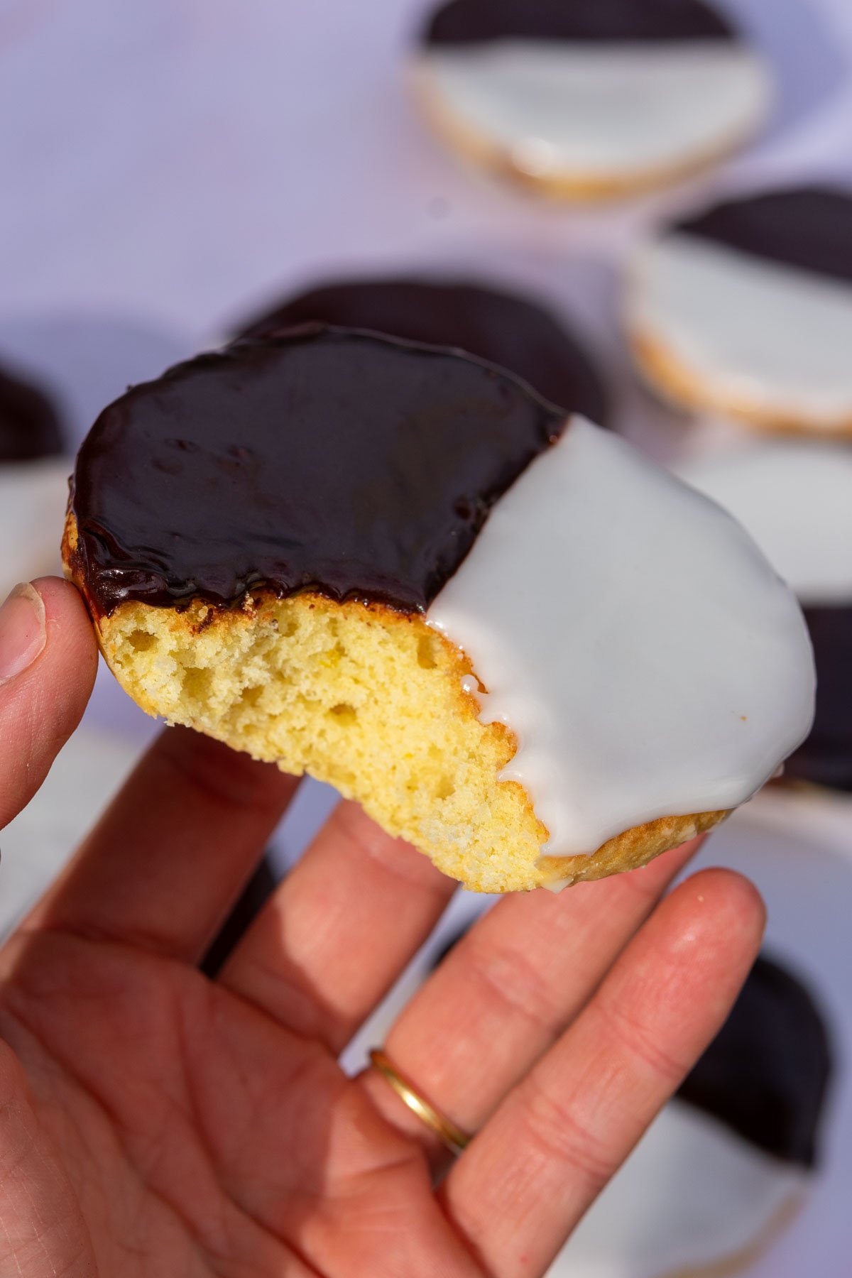 Hand holding a sourdough black and white cookie with a bite taken out of it.