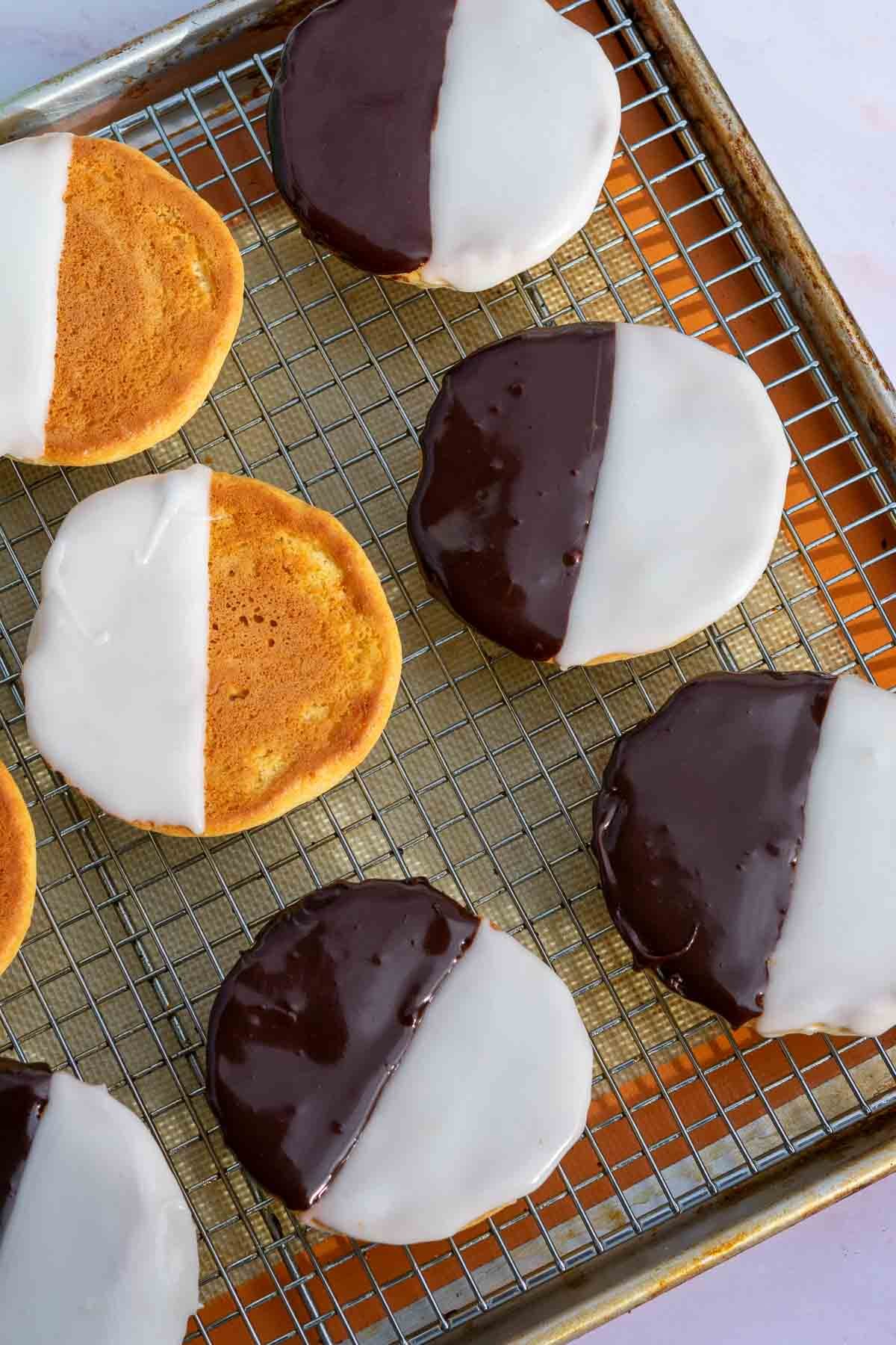 Sourdough black and white cookies setting on a wire rack with full icing on some and half iced on others.