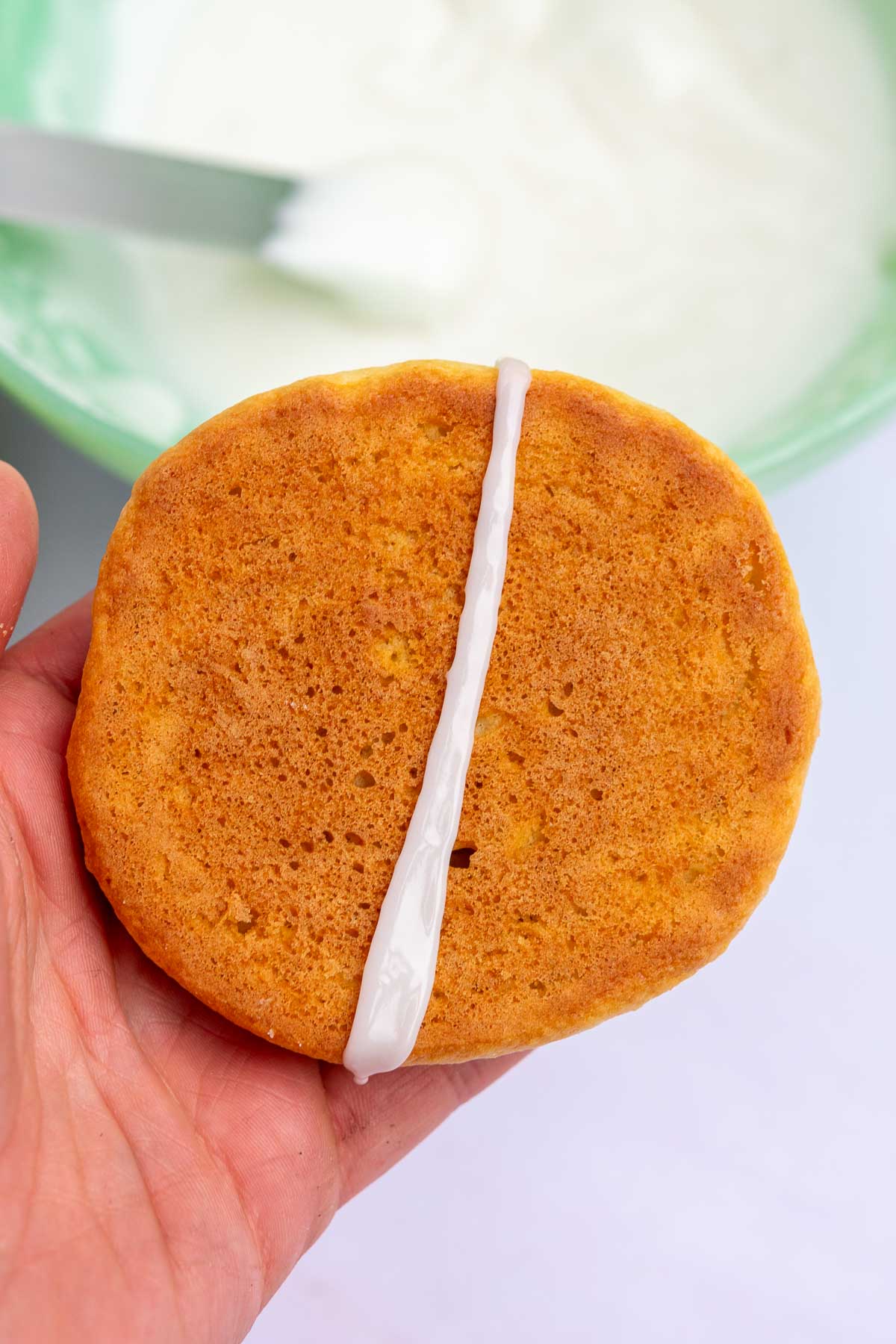 Hand holding a black and white cookie with a line of vanilla icing down the middle.