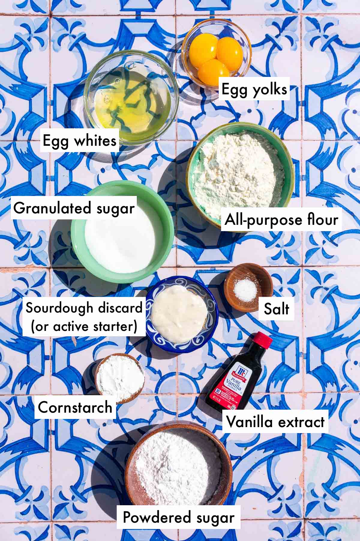 Labeled bowls of ingredients needed for sourdough ladyfingers including separated eggs, granulated sugar, all-purpose flour, salt, sourdough discard, vanilla extract, powdered sugar, and cornstarch.