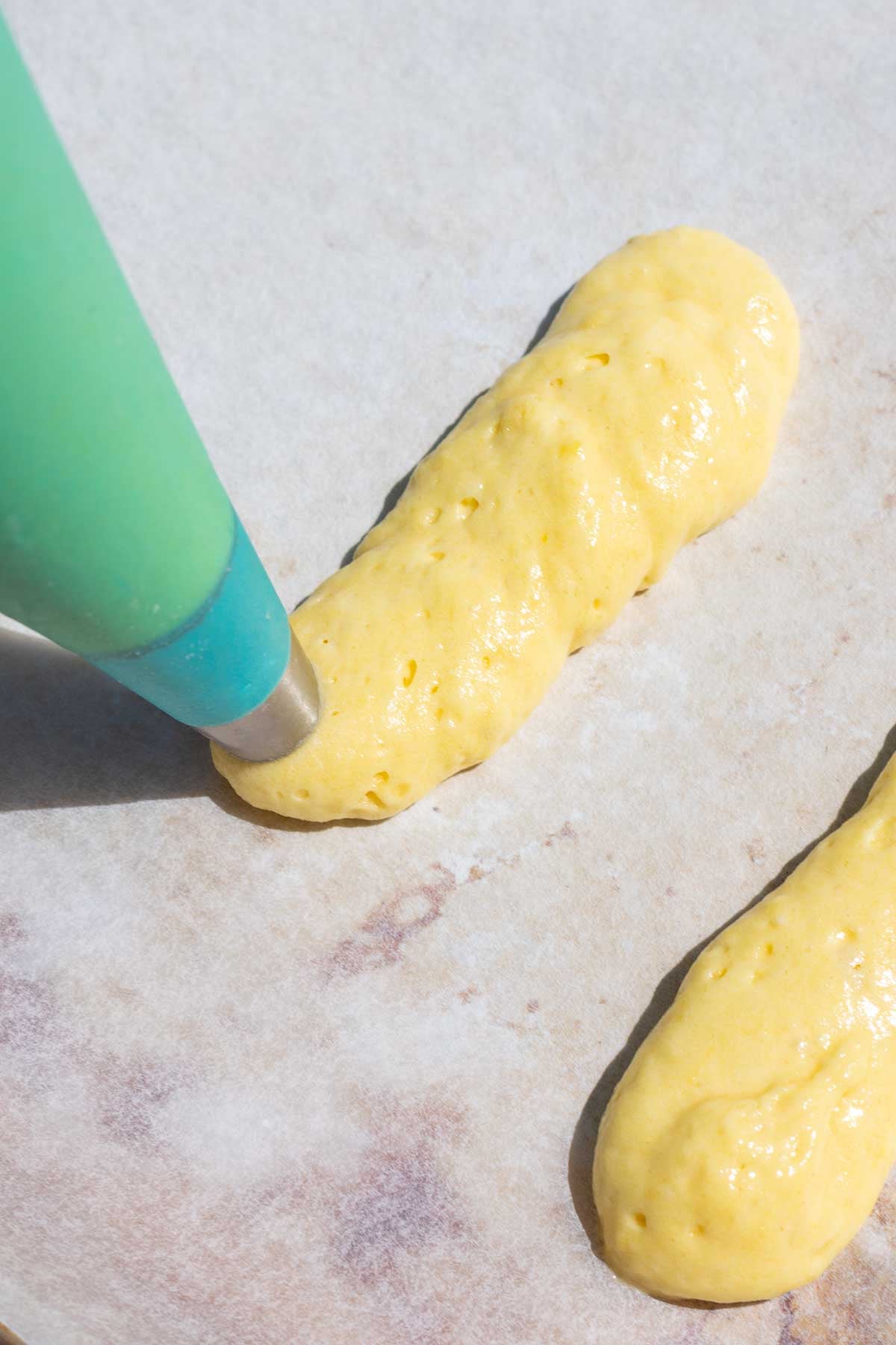 Piping sourdough ladyfingers on a baking sheet with parchment paper.
