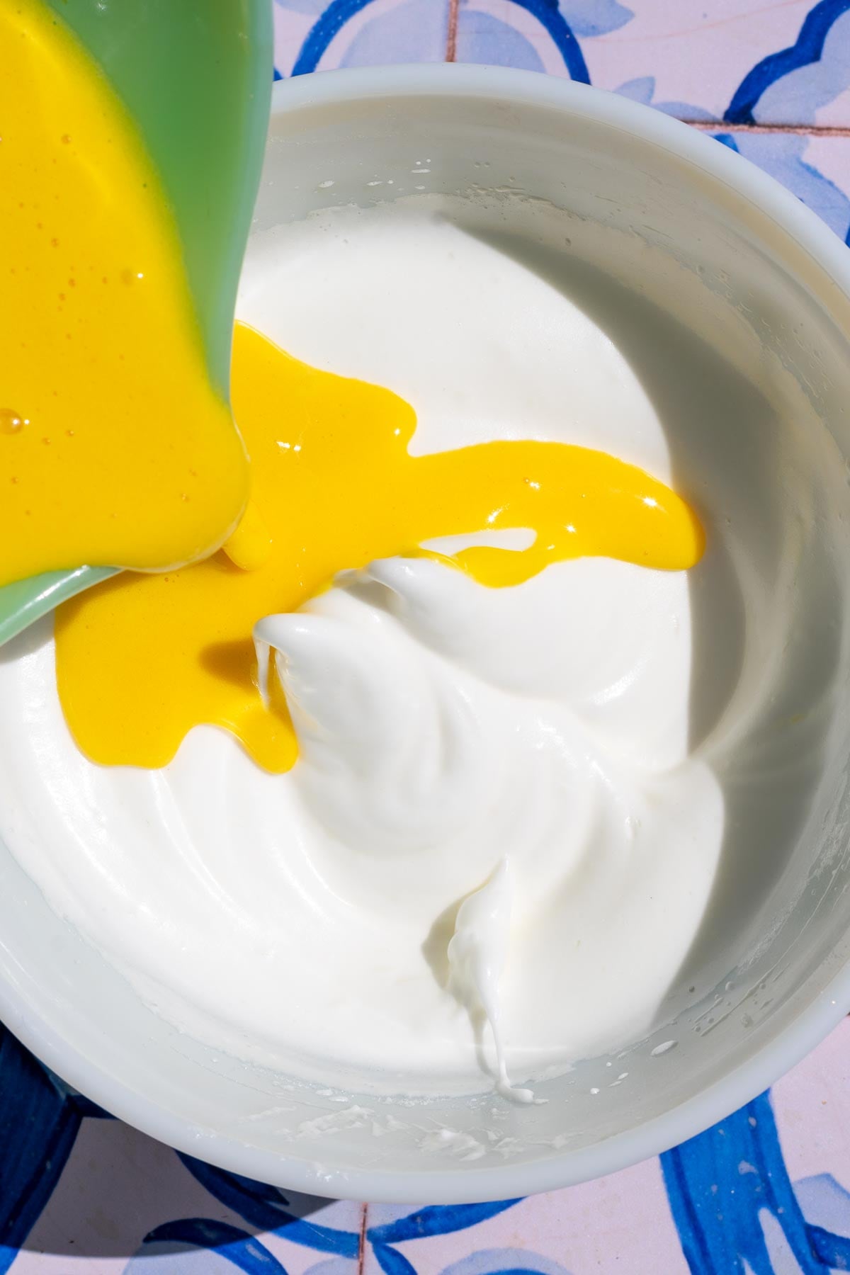 Pouring the egg yolk mixture into the whipped egg whites in a bowl.