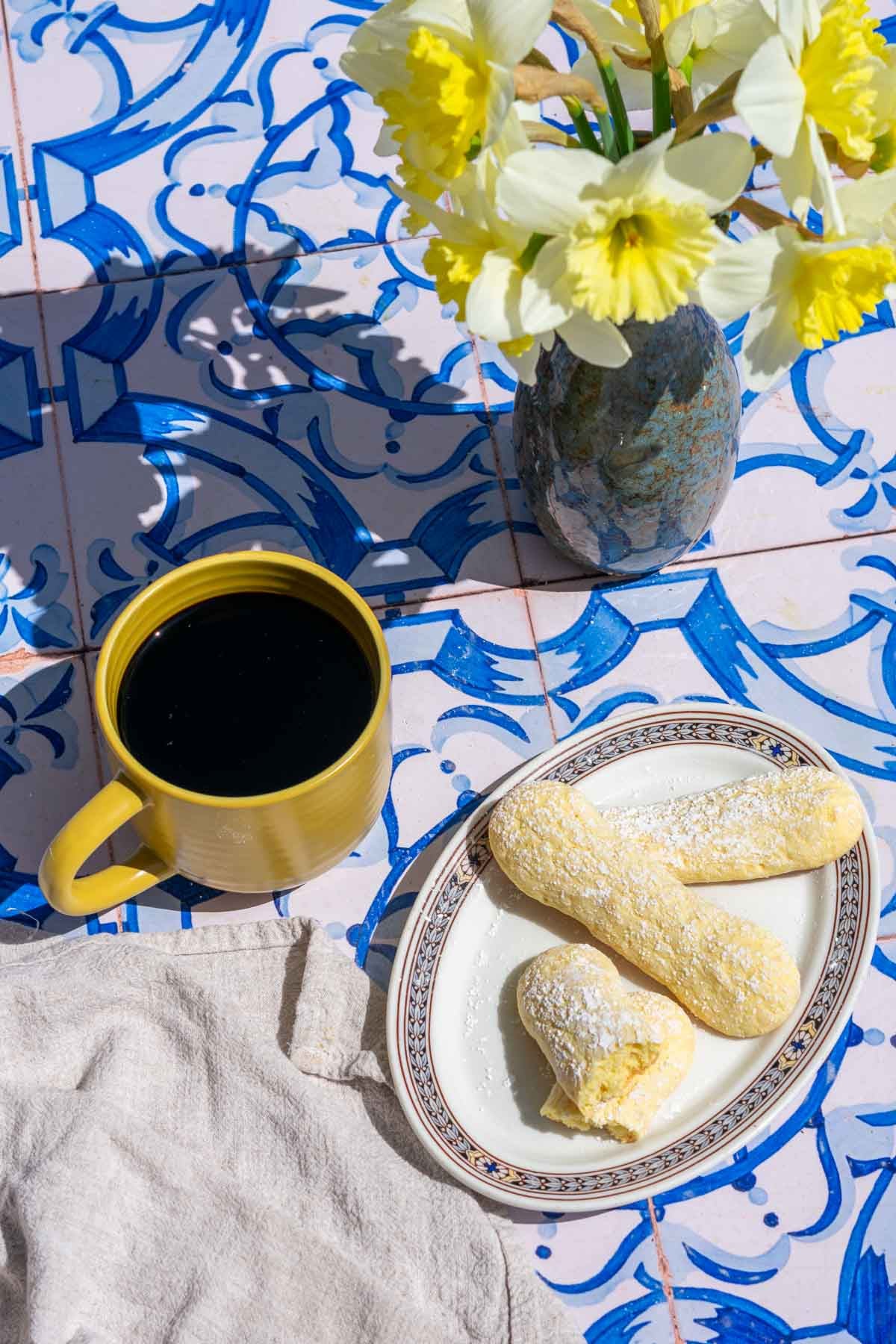 Sourdough ladyfingers on a plate with a mug of coffee and a vase of daffodils.