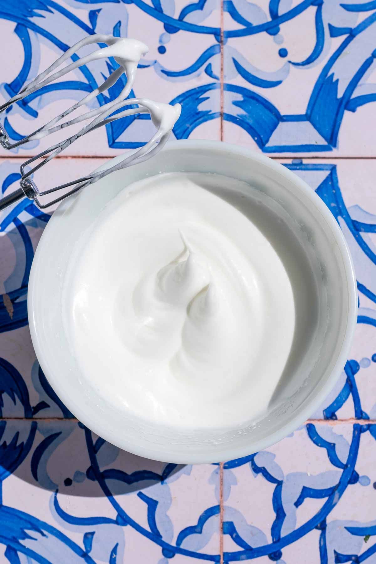 Whipped egg whites in a bowl to stiff peaks with an electric hand mixer to the side.