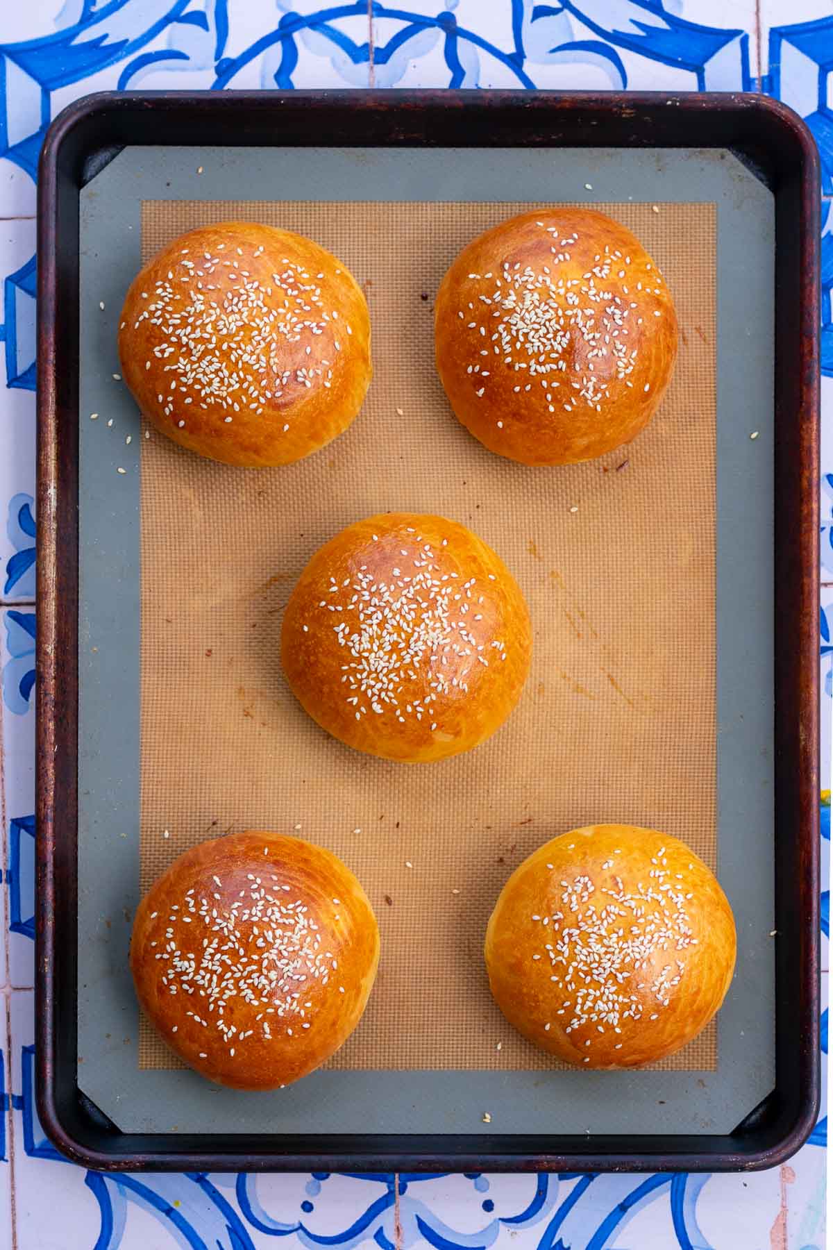 Baked sourdough brioche hamburger buns on a baking sheet.