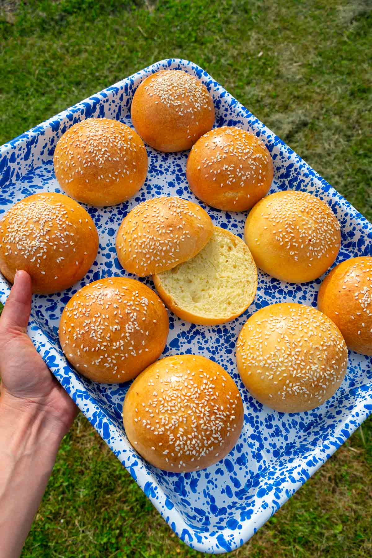 Hand holding a platter of sourdough brioche hamburger buns outside.