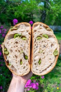 Hand holding sliced olive sourdough bread sliced in half.