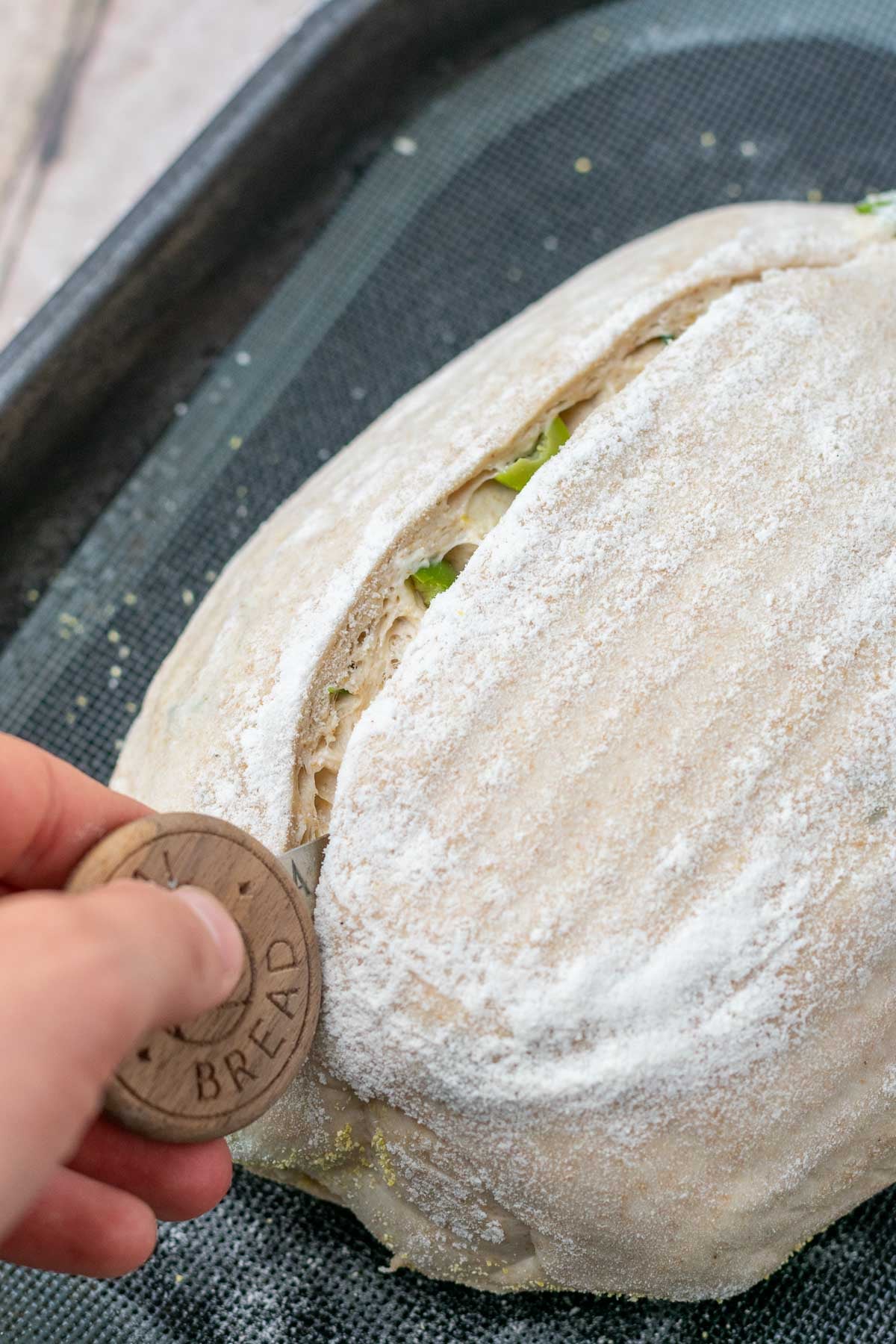 Scoring olive sourdough bread with a bread lame.