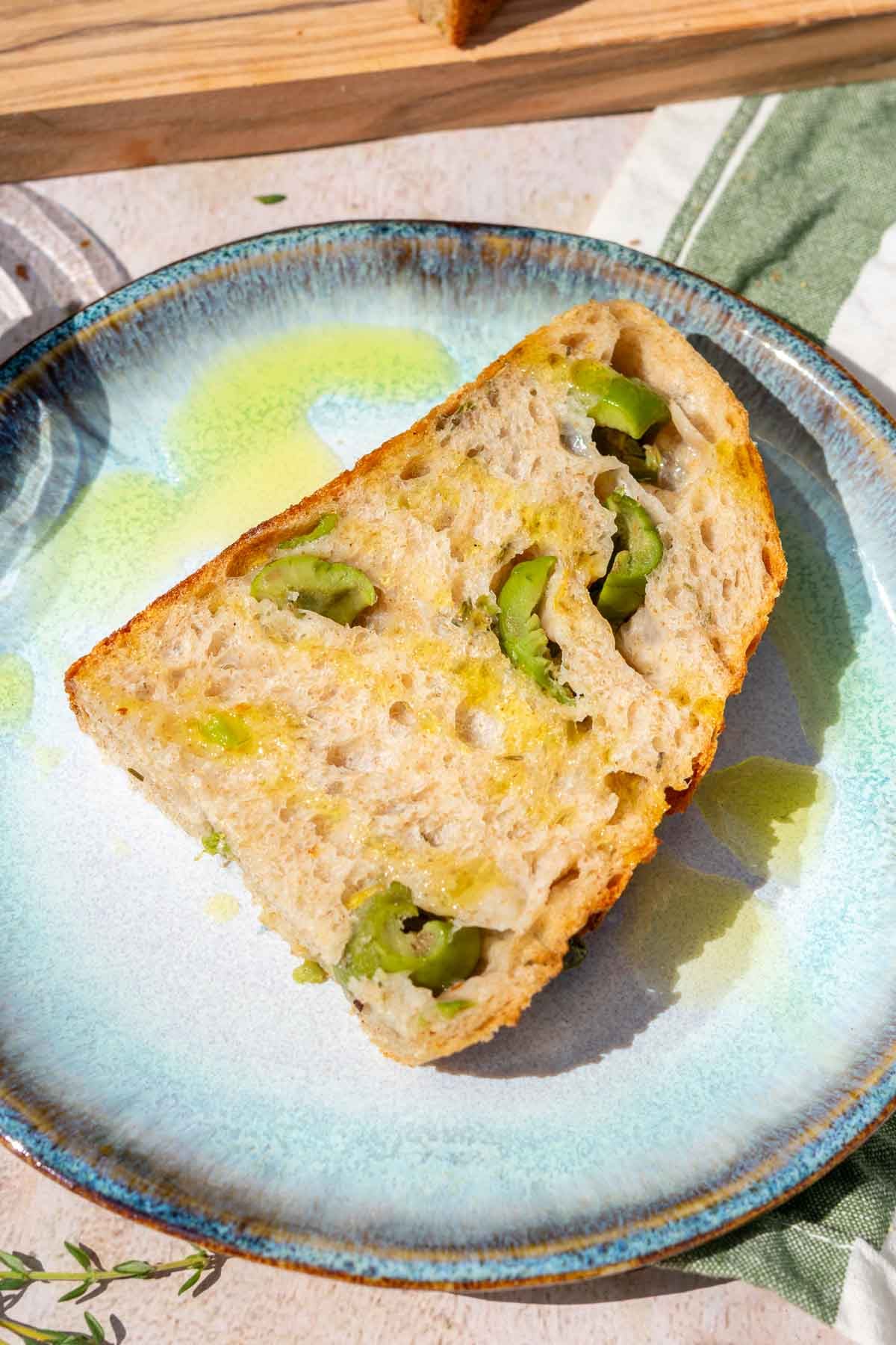 Slice of olive sourdough bread on a plate with a drizzle of olive oil.