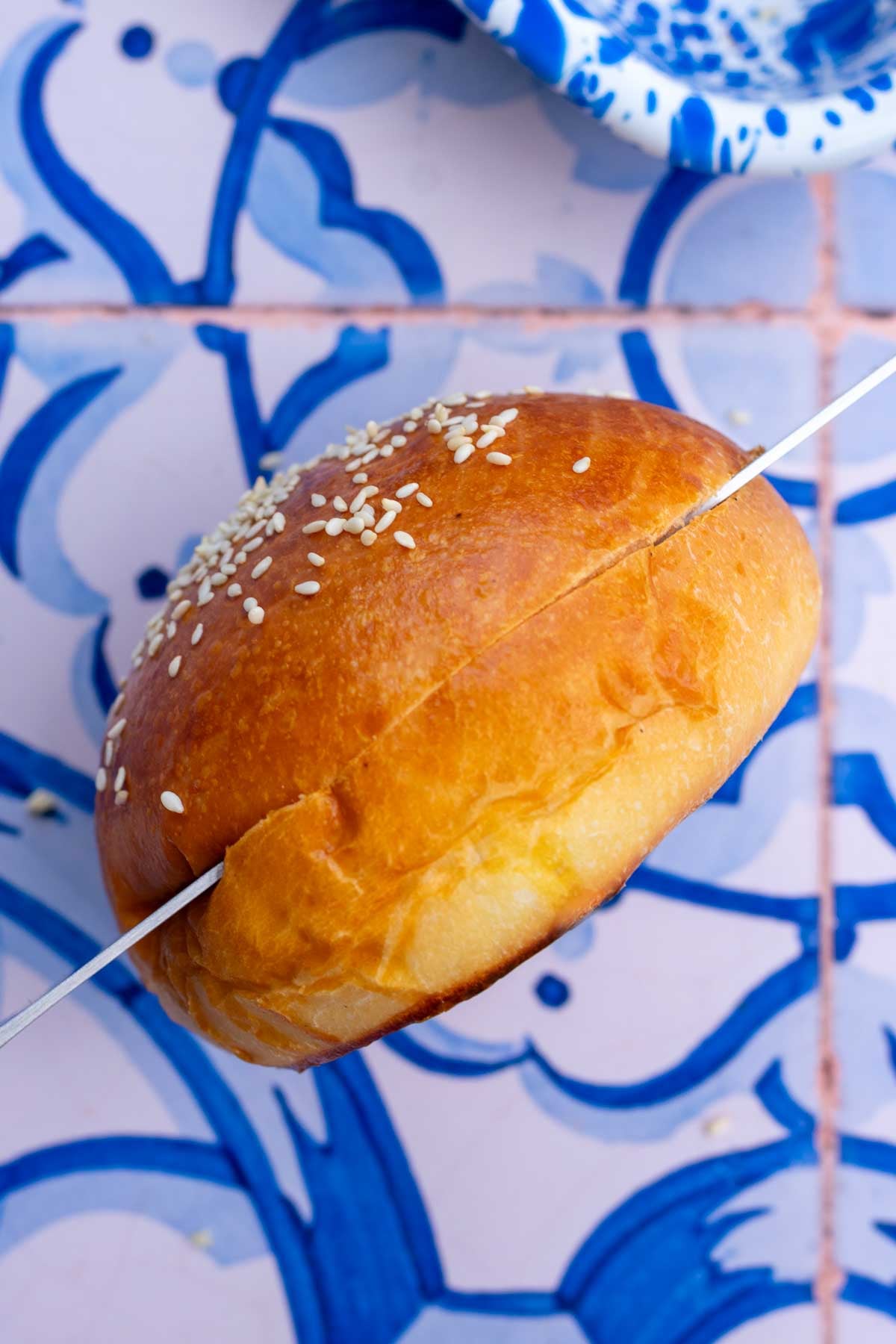 Slicing a sourdough hamburger bun with a bread knife in half.