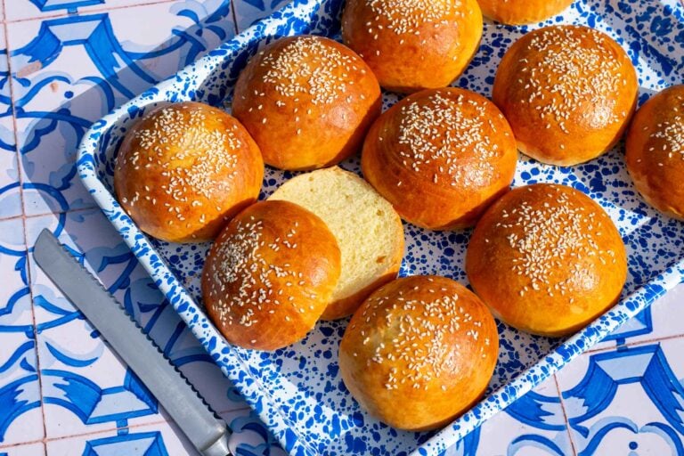 Enamel platter of sourdough brioche hamburger buns topped with sesame seeds and a bread knife.