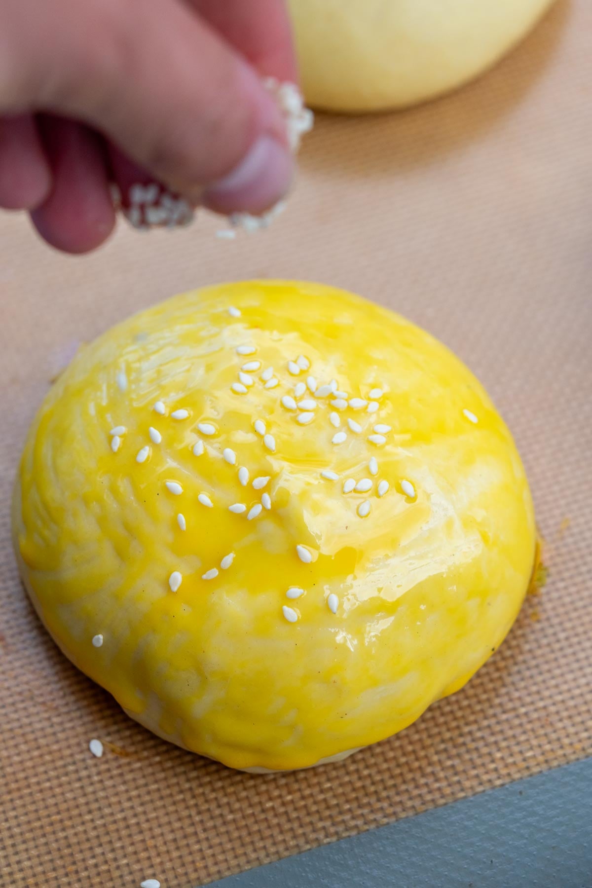Sprinkling sesame seeds on top of sourdough hamburger buns.