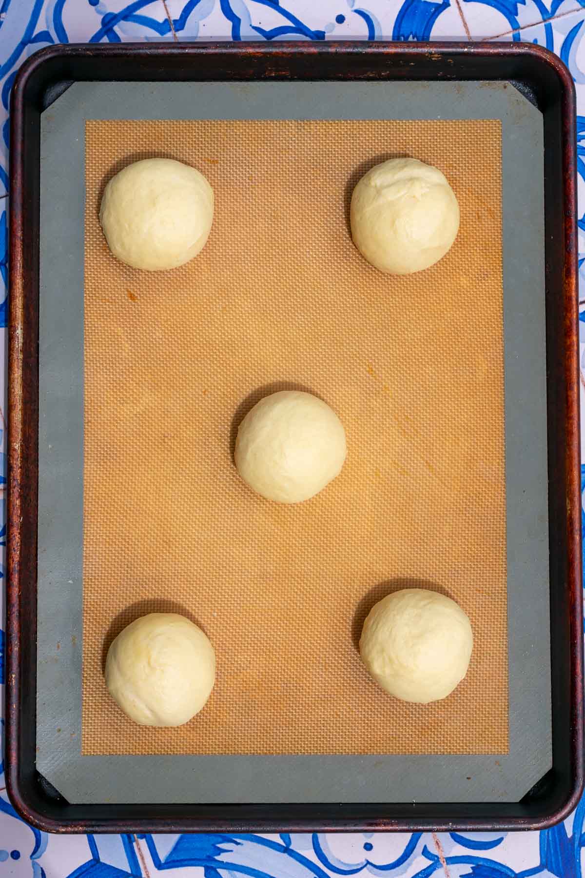 Five sourdough brioche hamburger buns on a baking sheet at the start of final proofing.