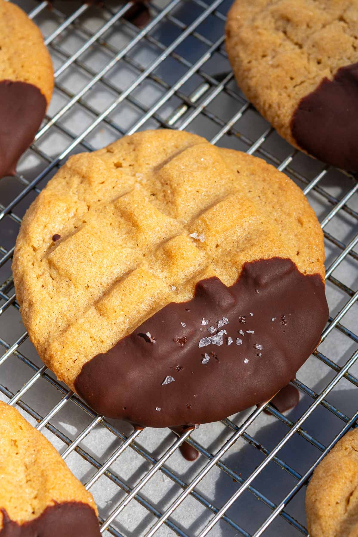 A chocolate dipped sourdough peanut butter cookie on a cooling rack.