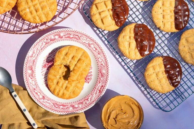 Chocolate dipped sourdough peanut butter cookies on a wire rack and a plate of cookies with a bowl of peanut butter.