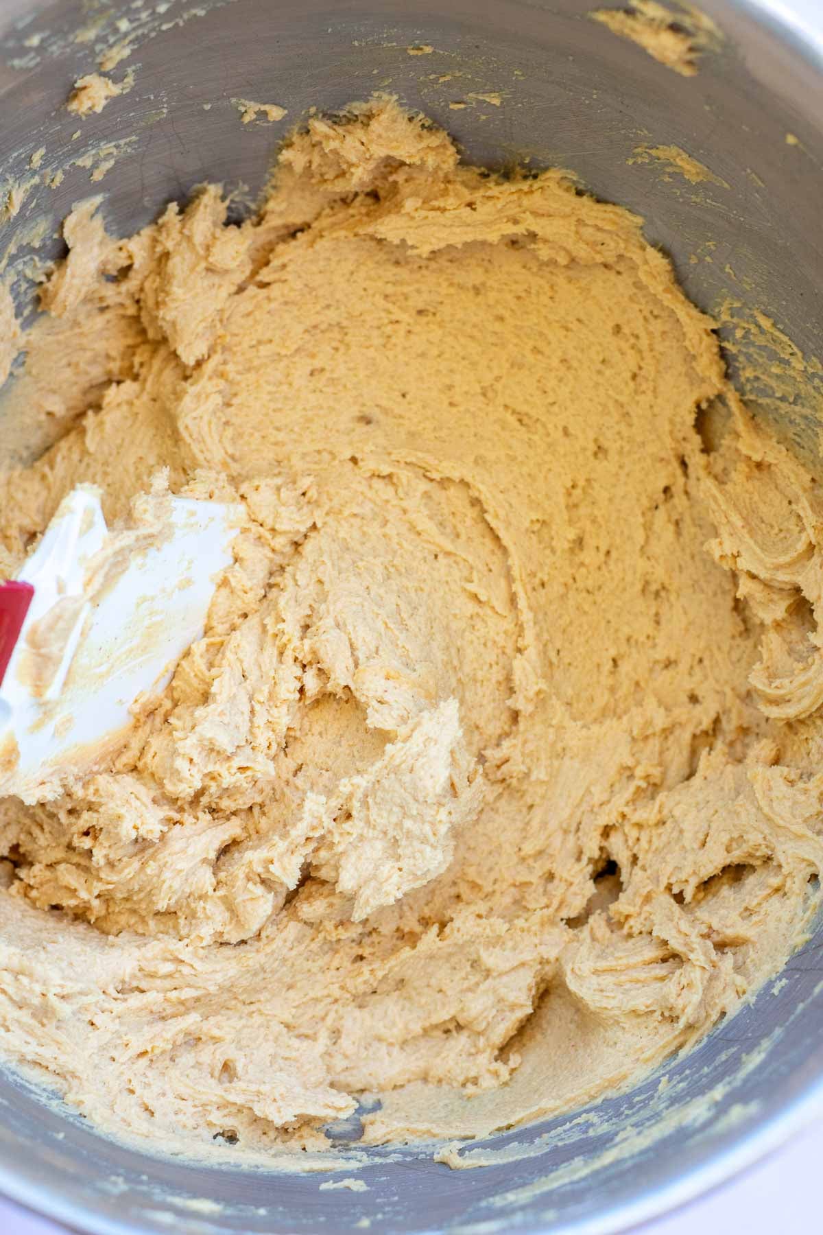 Stand mixer bowl with mixed sourdough peanut butter cookie dough and a spatula.