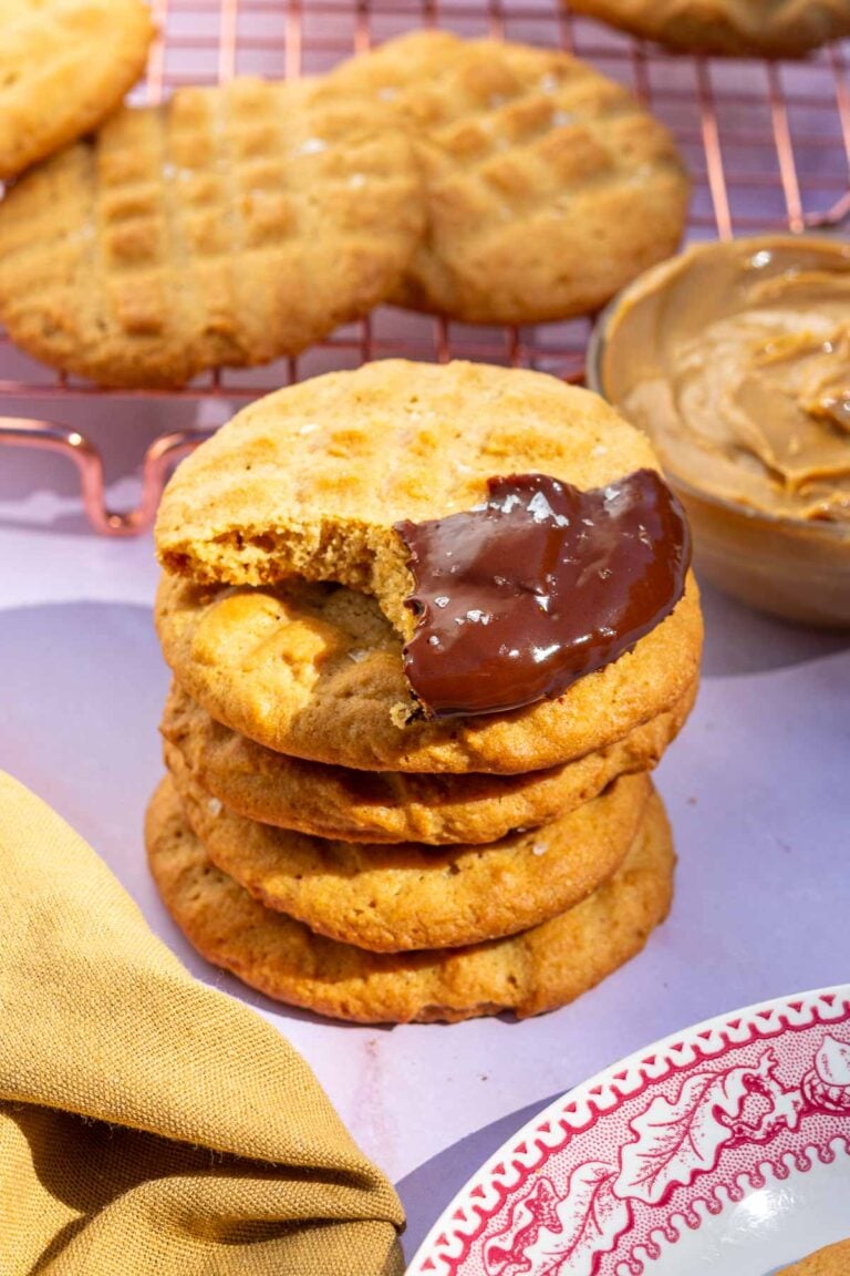 Stack of sourdough peanut butter cookies with the top one with a bite taken out of it and dipped in chocolate.
