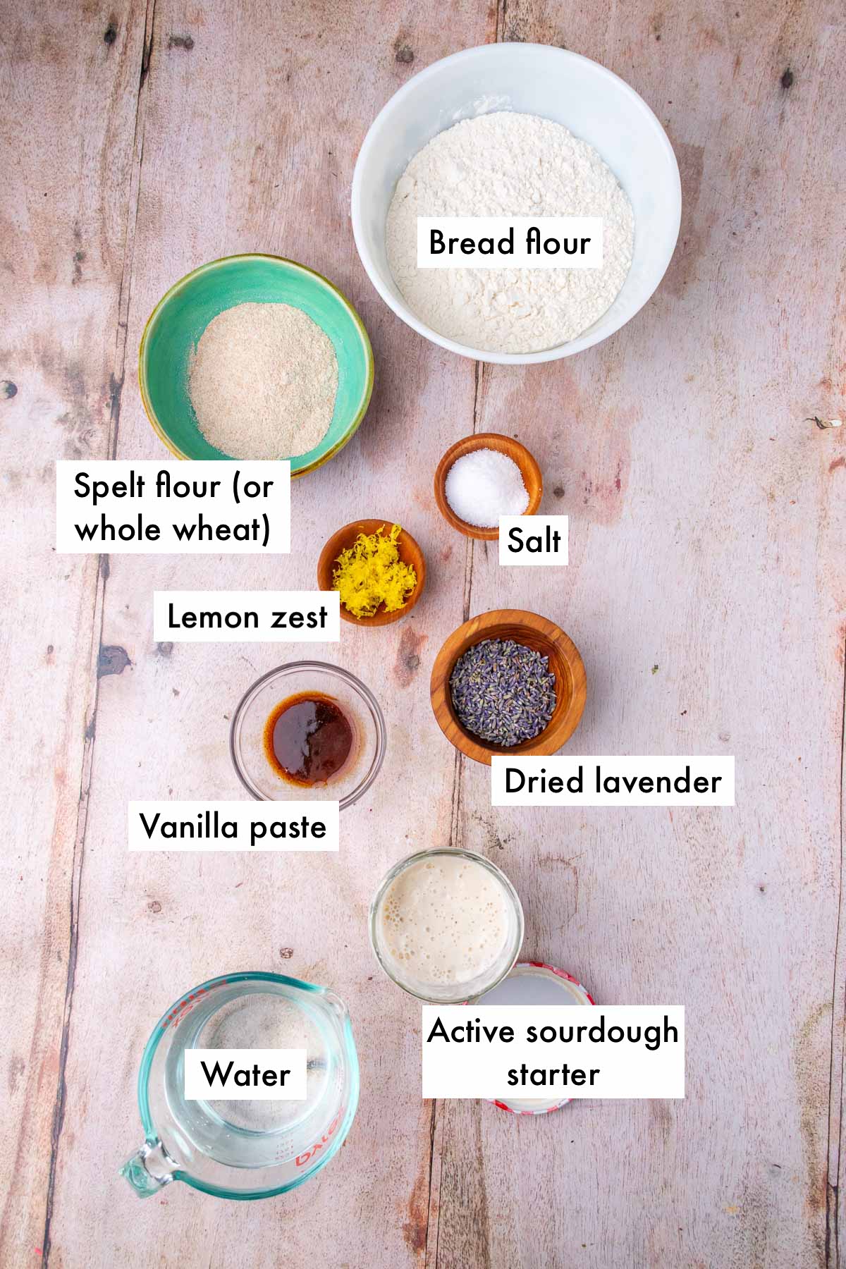 Labeled bowls of ingredients needed for lavender sourdough bread including bread flour, spelt flour (or whole wheat), salt, lemon zest, lavender, vanilla paste, sourdough starter, and water.