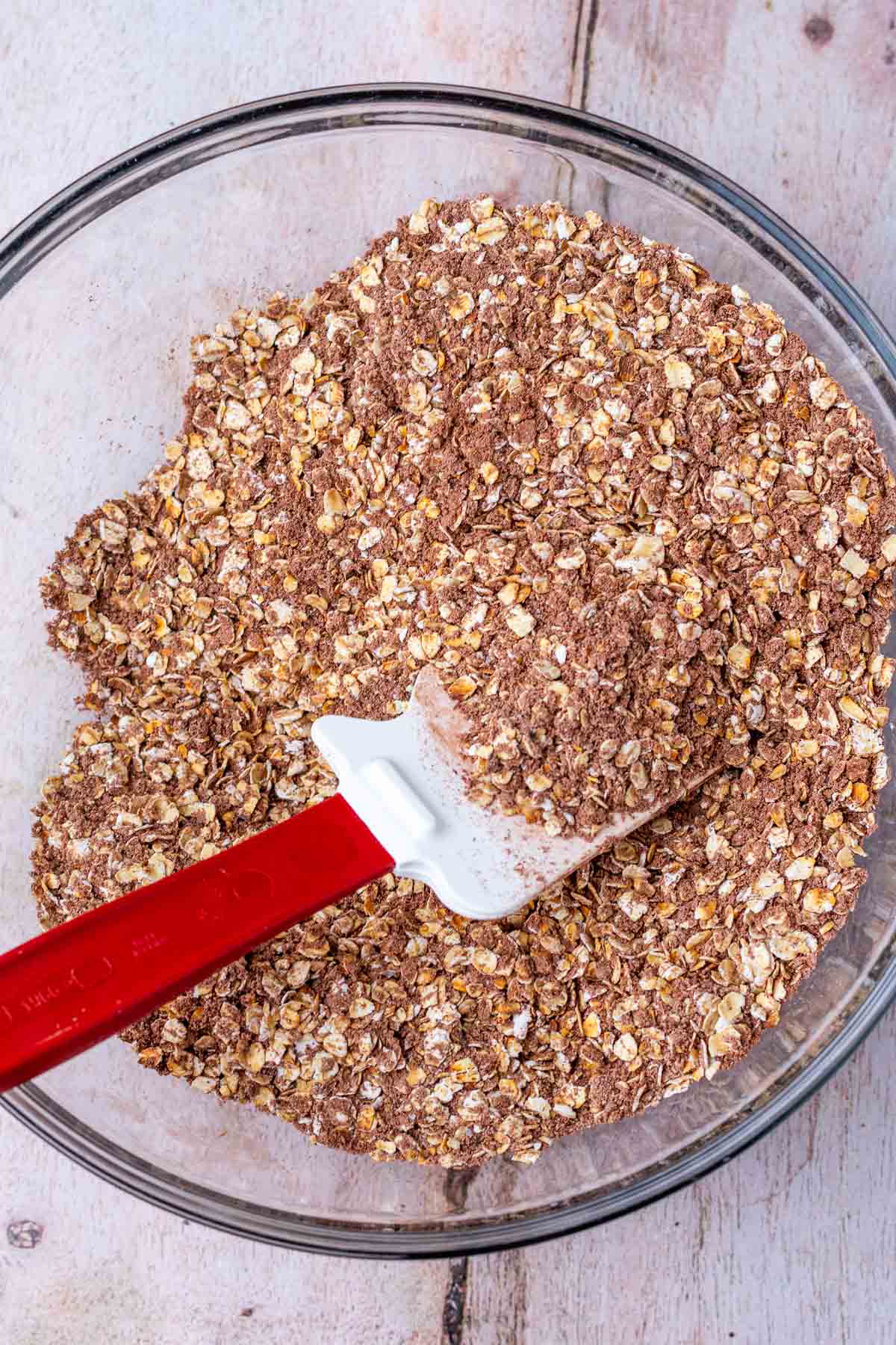 Mixing dry ingredients for granola bars in a bowl with a spatula.