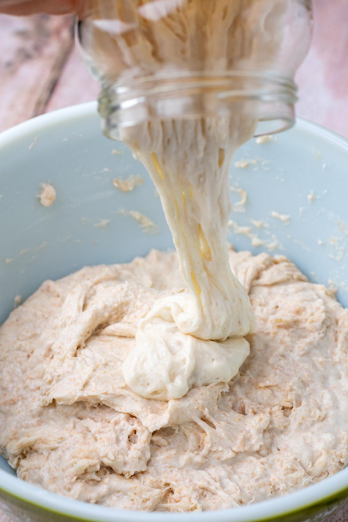 Pouring levain starter into a bowl of dough.